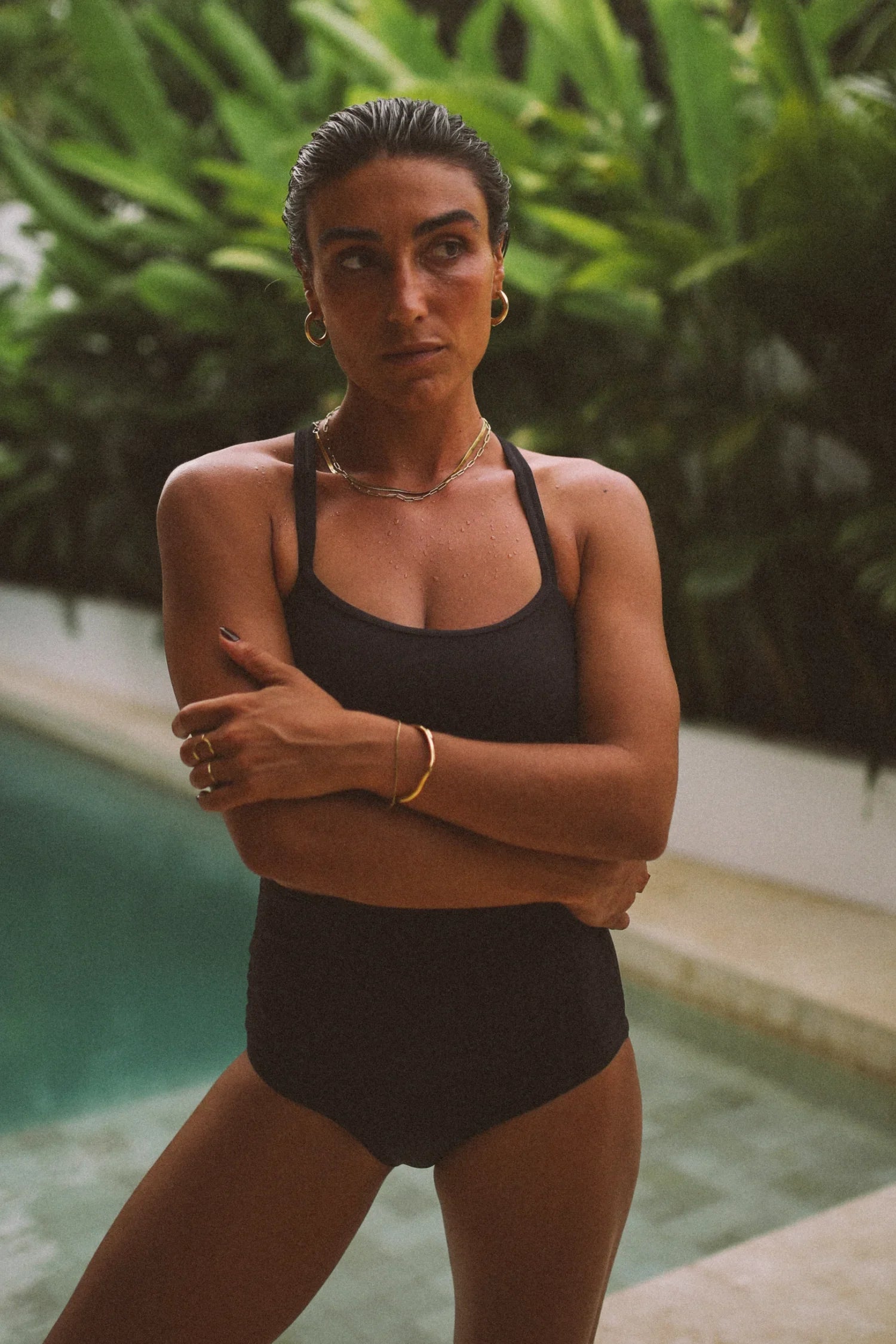 Frau im schwarzen Badeanzug steht nass vor tropischen Pflanzen am Pool.