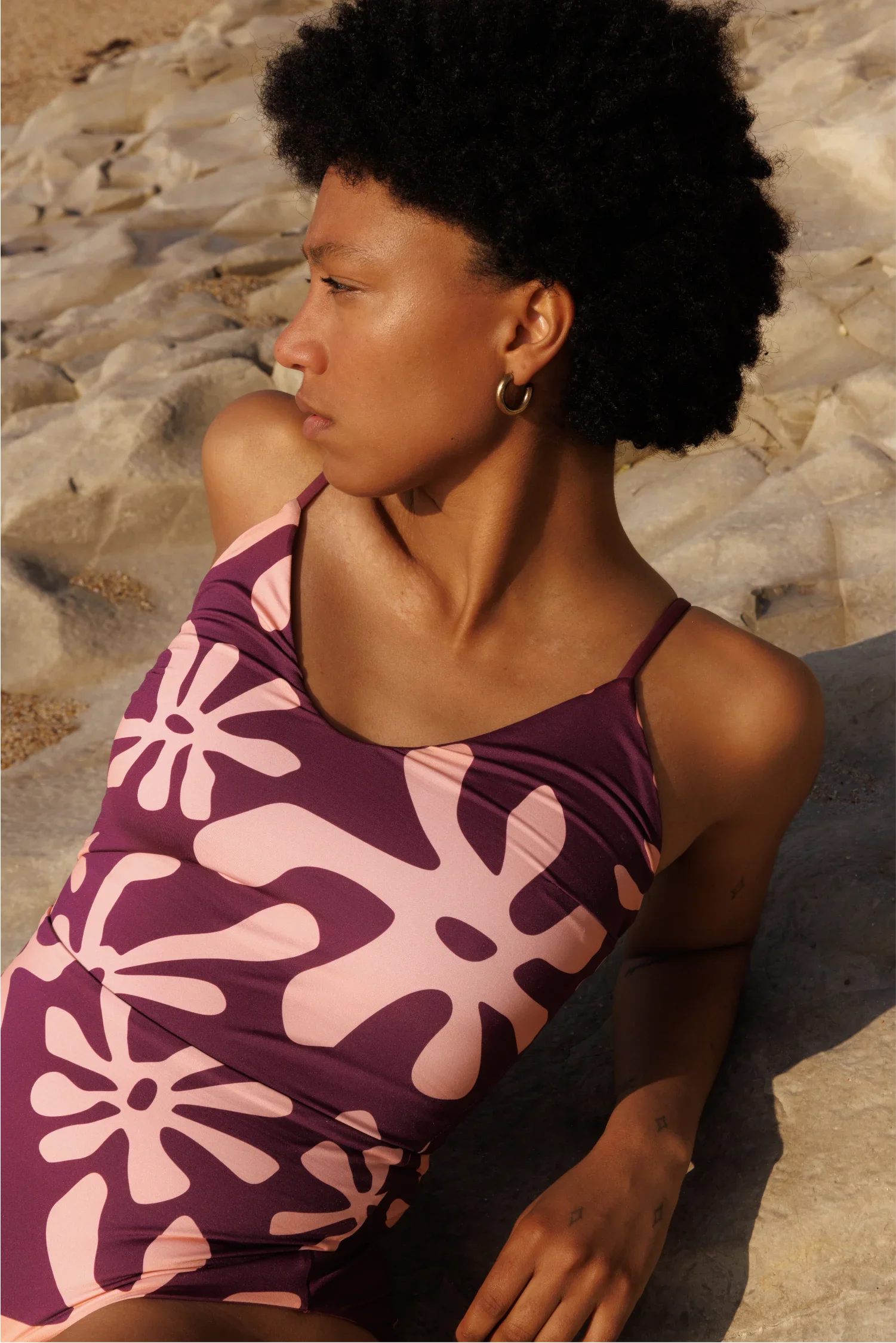 Frau liegt auf Felsen und trägt gemusterten Badeanzug in Bordeaux.