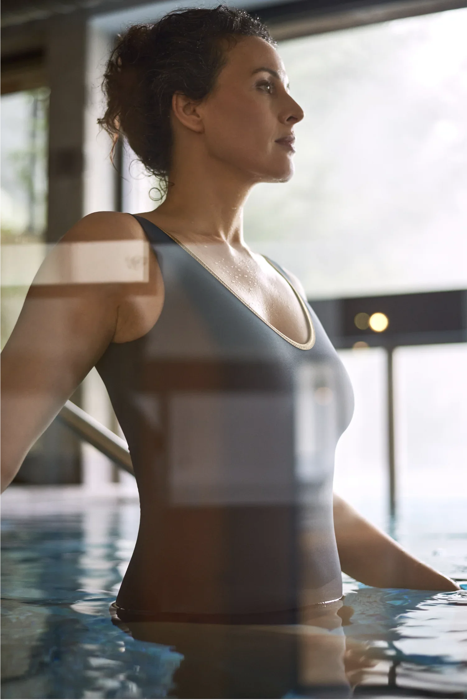 Frau im Badeanzug steht im Innenpool und blickt ruhig nach vorne.