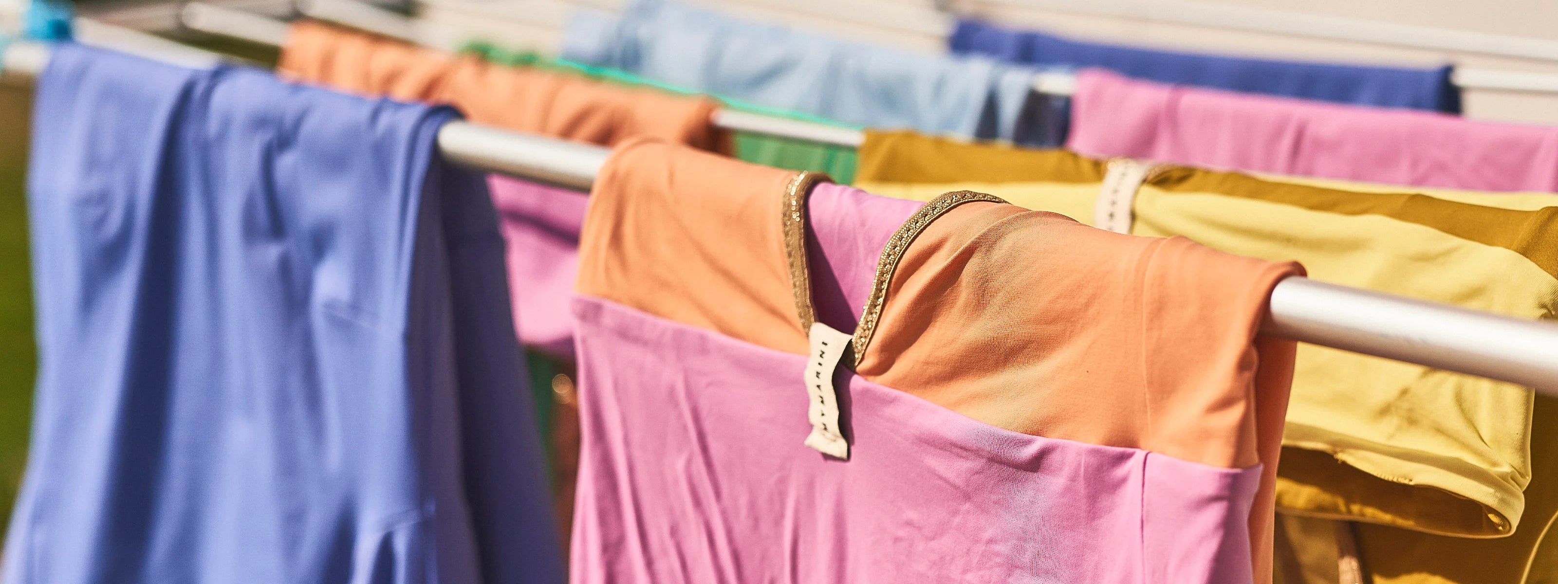 Bunte MYMARINI-Badeanzüge mit breiten Trägern hängen auf einer Wäscheleine in der Sonne.