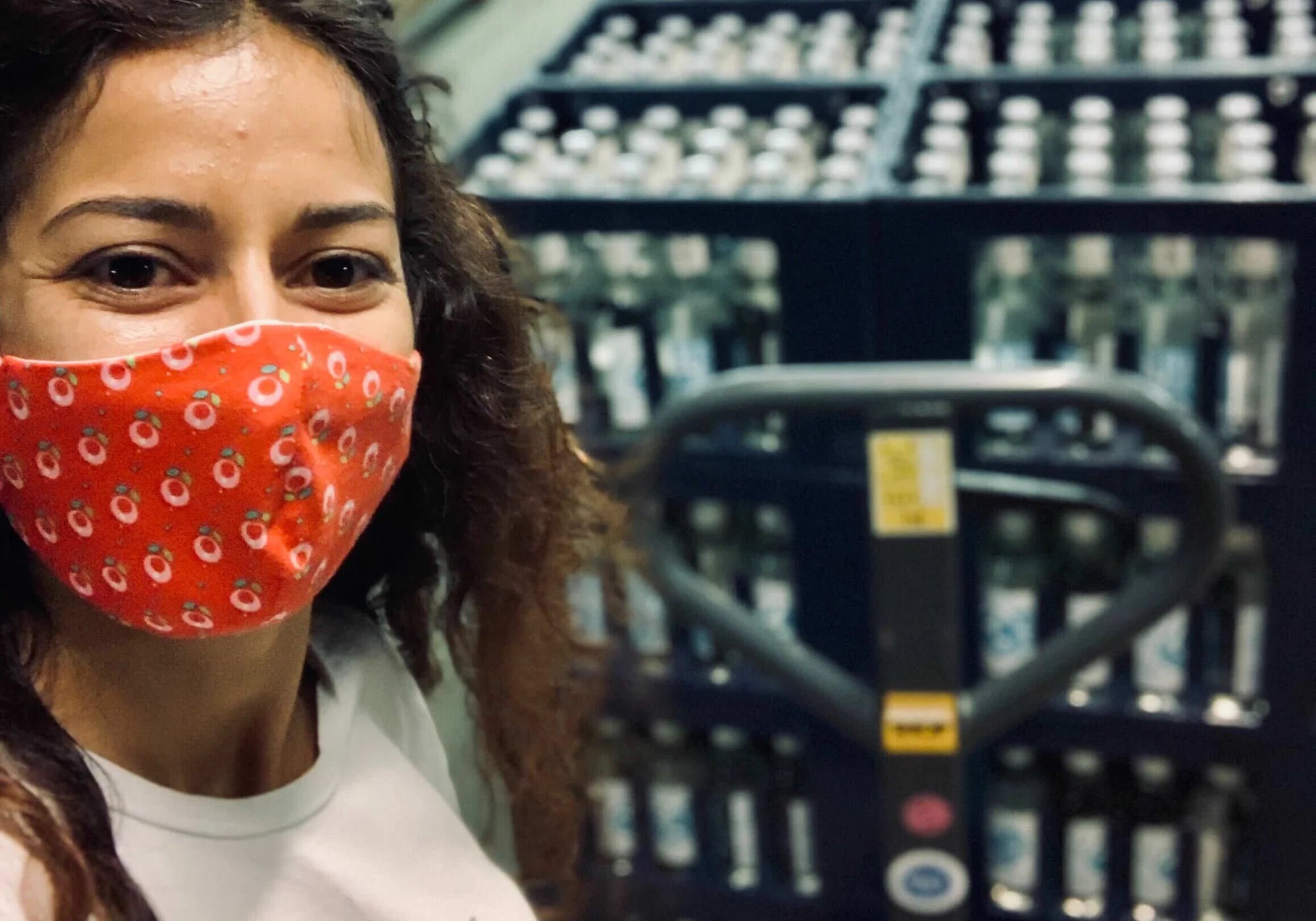 Eine Person mit roter Maske steht vor einem Stapel Wasserflaschen auf einem Palettenwagen.