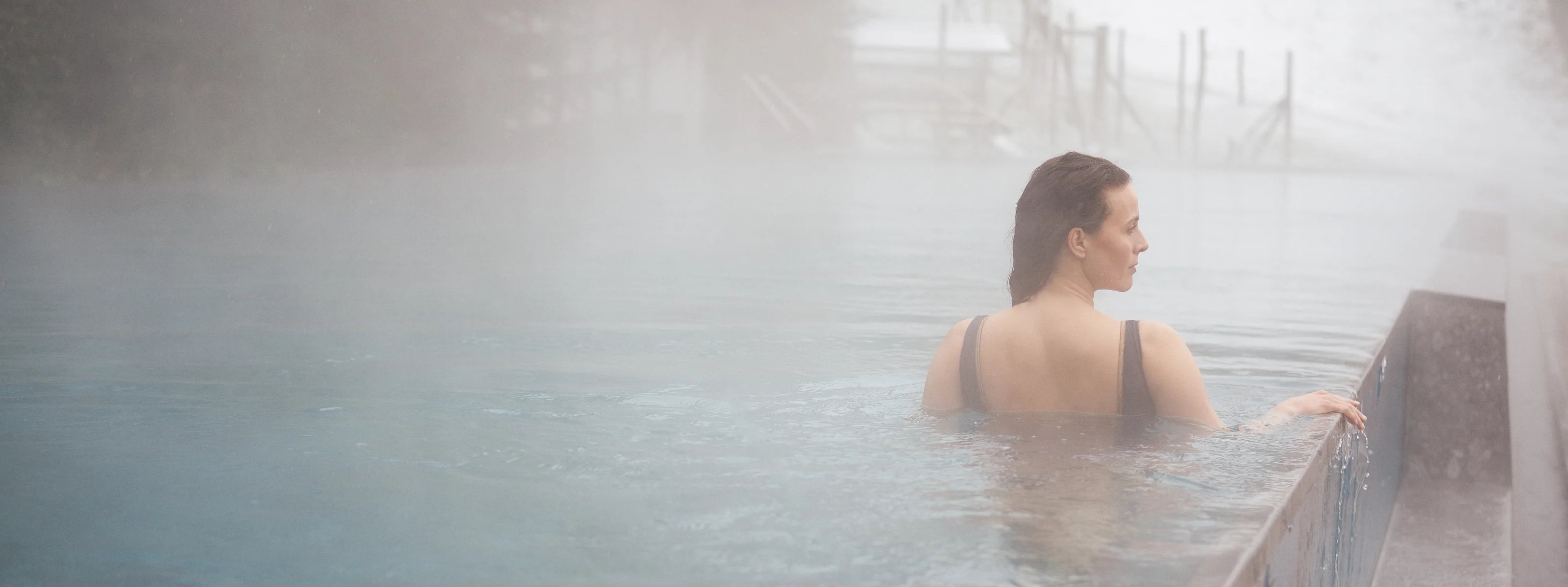 Person in einem MYMARINI Badeanzug mit breiten Trägern im Pool, umgeben von Nebel.