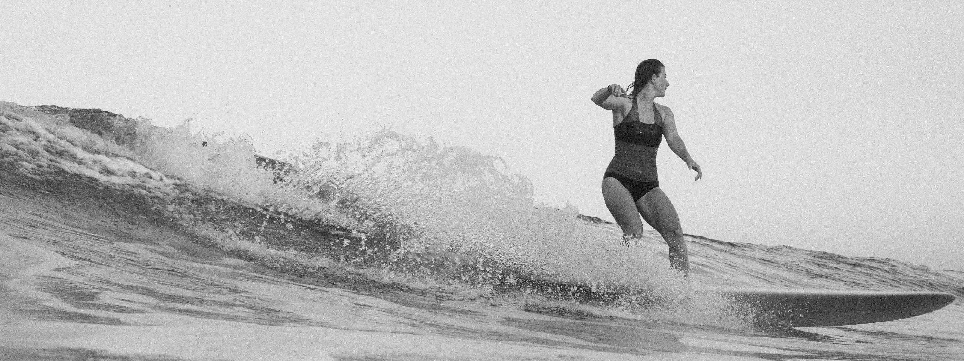 Person surft auf einer Welle in einem MYMARINI-Bikinitop mit breiten Trägern und Bikinihose.