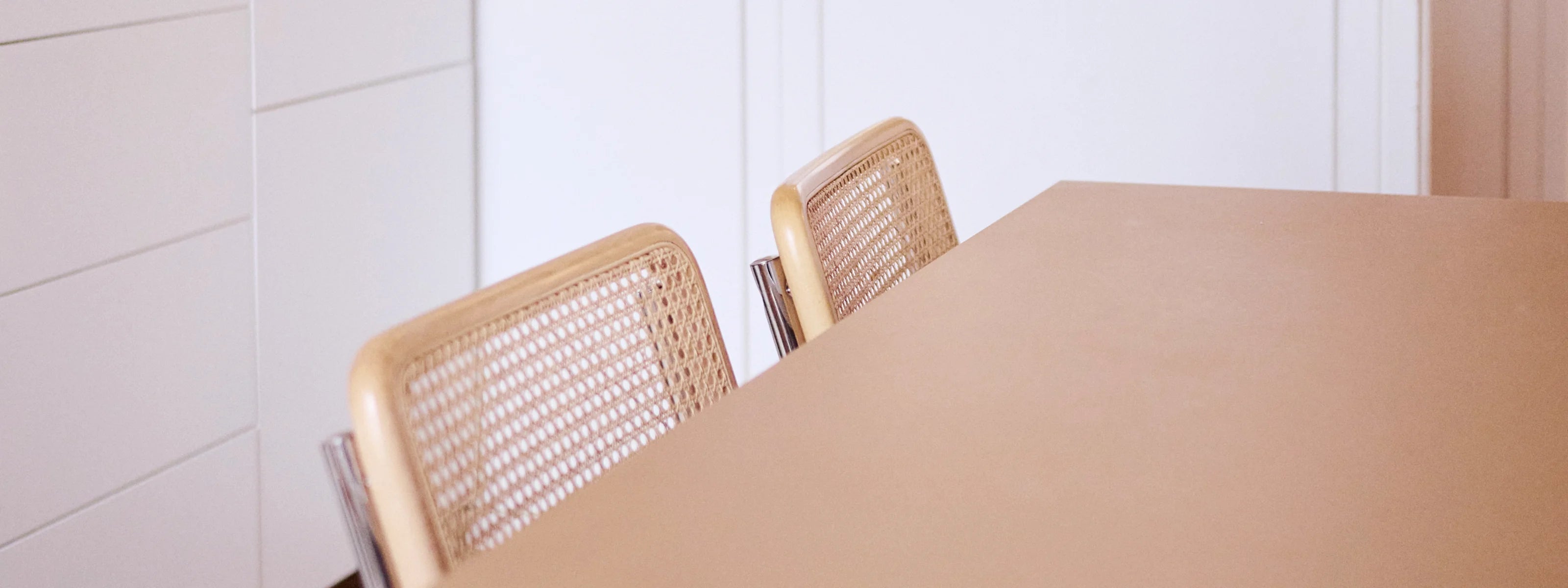 Zwei Holzstühle mit geflochtener Rückenlehne an einem Tisch in einem minimalistischen Raum.