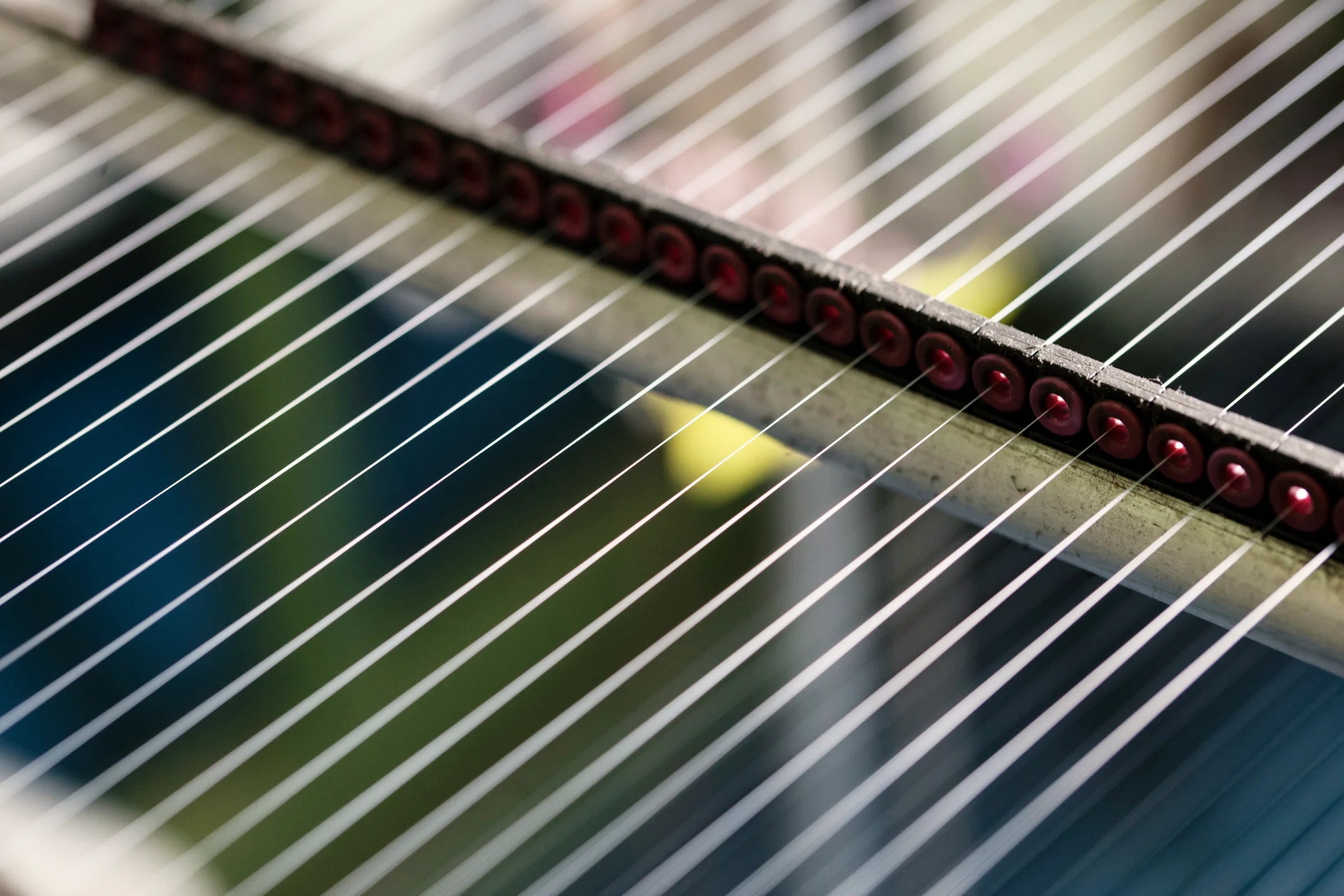 Detailaufnahme gespannter Garnfäden in einer textilen Produktionsanlage, geführt durch eine Reihe roter Umlenkrollen.