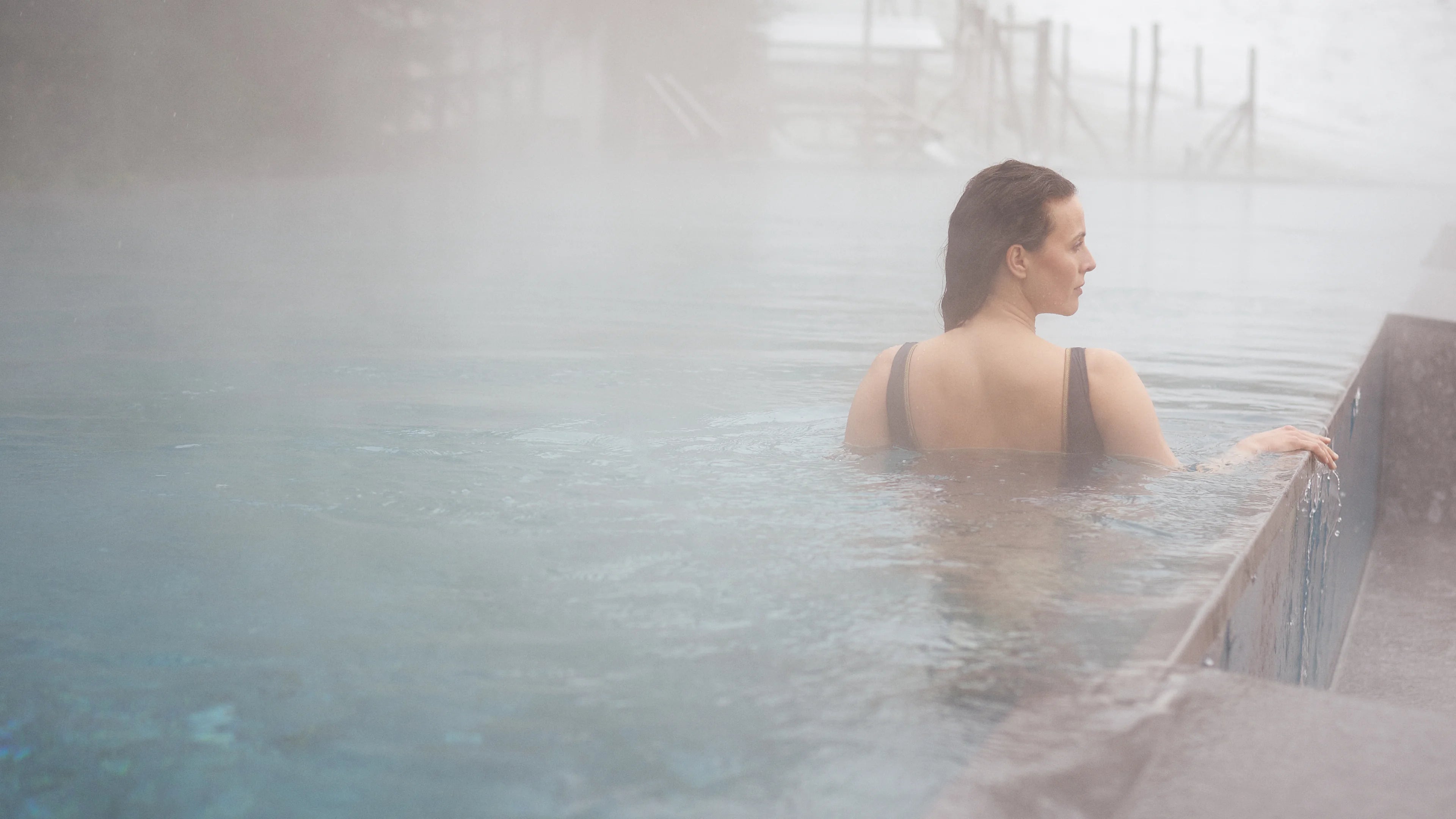 Person in einem MYMARINI Badeanzug mit breiten Trägern im dampfenden Pool, schaut zur Seite.
