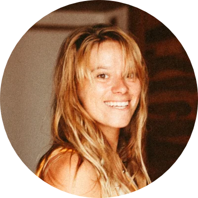 Lächelnde Frau mit blonden Haaren steht drinnen vor warmem Hintergrund.