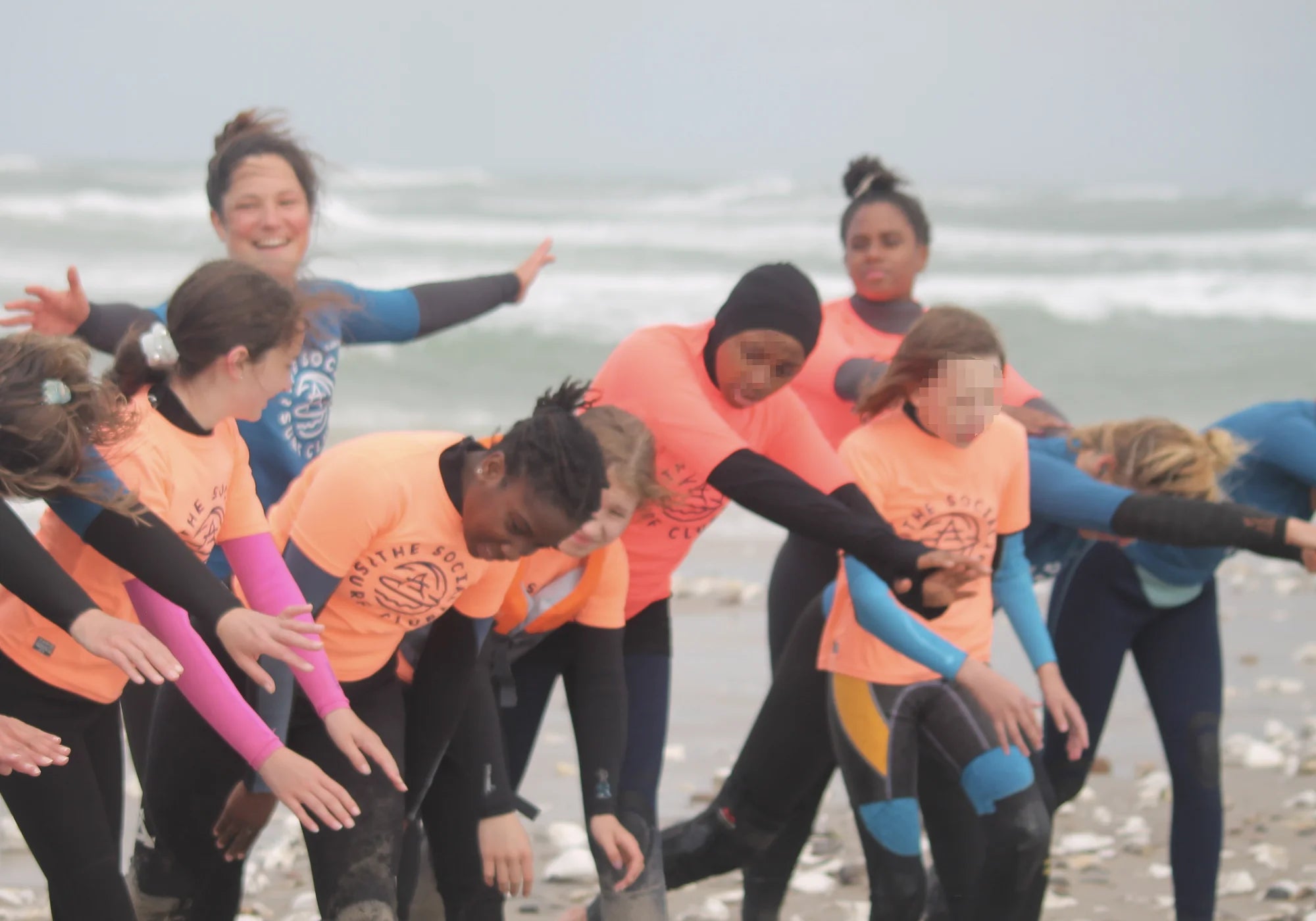 Eine Gruppe von Menschen in Neoprenanzügen und bunten T-Shirts übt am Strand Surfen.