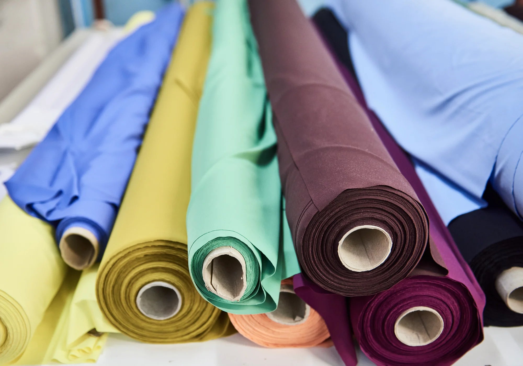 Verschiedene Stoffrollen in bunten Farben liegen nebeneinander auf einem Tisch.