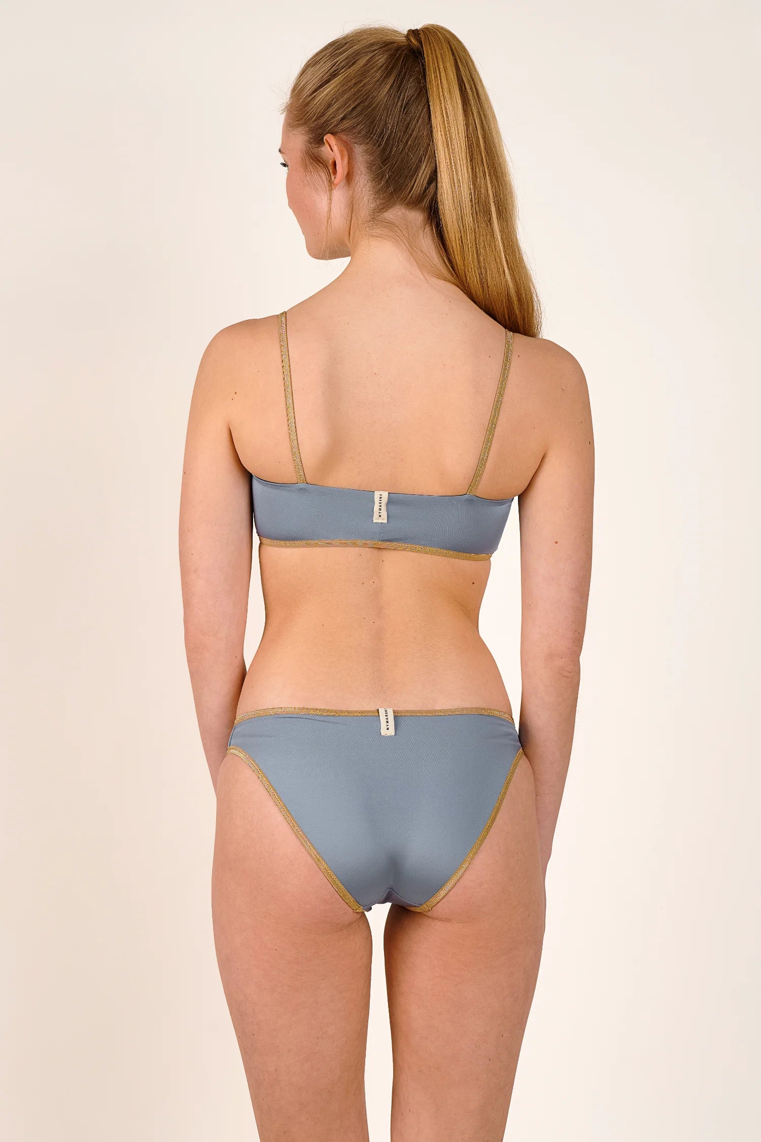 Bikini-Top und -Hose von MYMARINI in Grau mit schmalen Trägern und goldenen Akzenten, von hinten fotografiert.#color_crystal-grey
