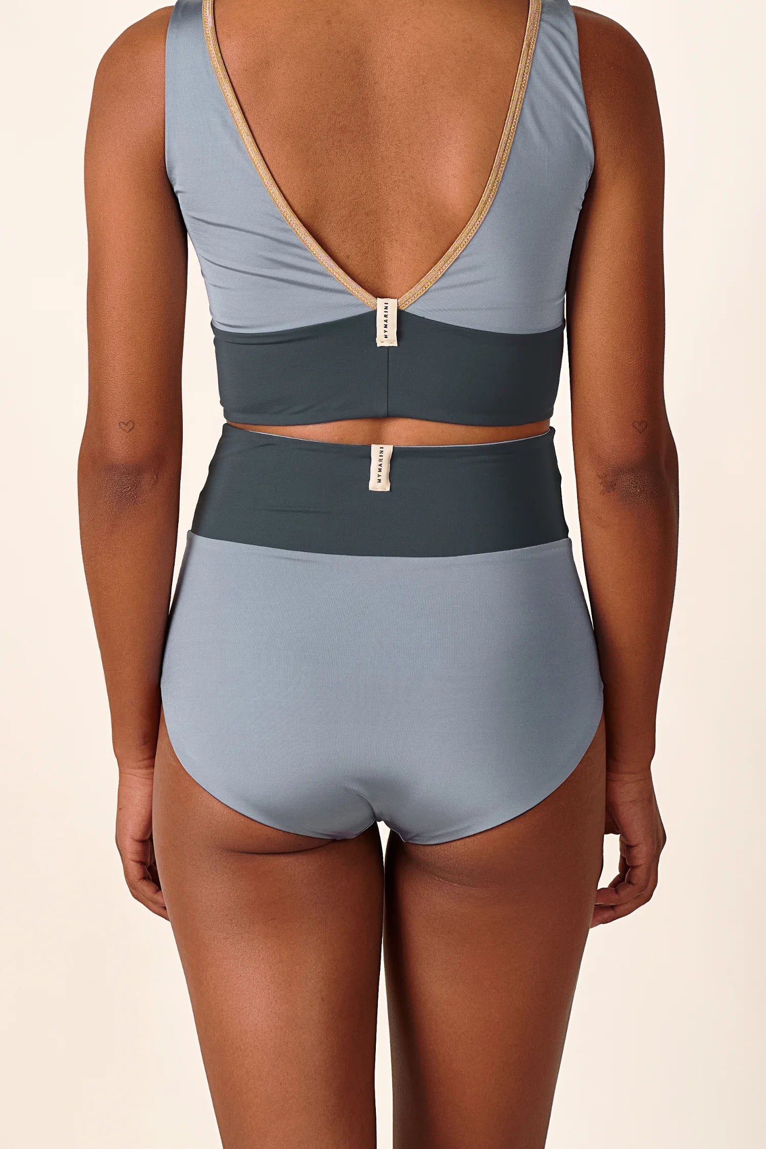 Rückansicht einer Person in einem MYMARINI Bikini mit V-Ausschnitt und High Waist Schnitt in Blau und Dunkelgrau.#color_crystal-grey
