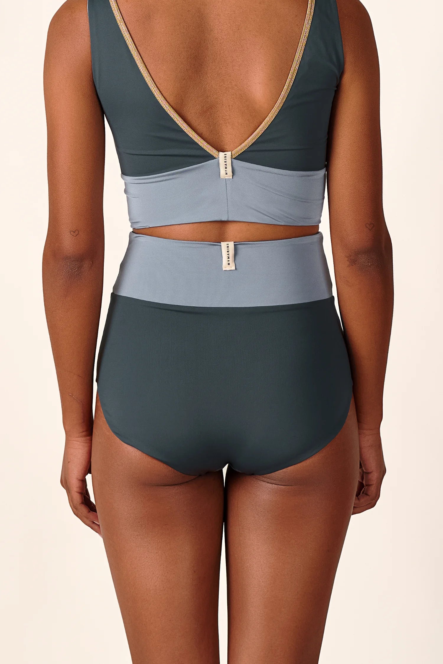 Rückansicht einer Person in einem MYMARINI Bikini mit V-Ausschnitt und hohem Beinausschnitt in Dunkel- und Hellgrau.#color_crystal-grey