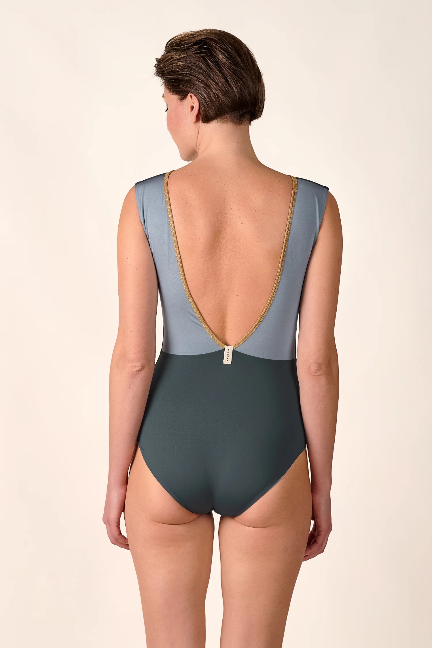 Person trägt einen MYMARINI Badeanzug mit tiefem Rückenausschnitt und breiten Trägern in Blau- und Grüntönen.#color_crystal-grey