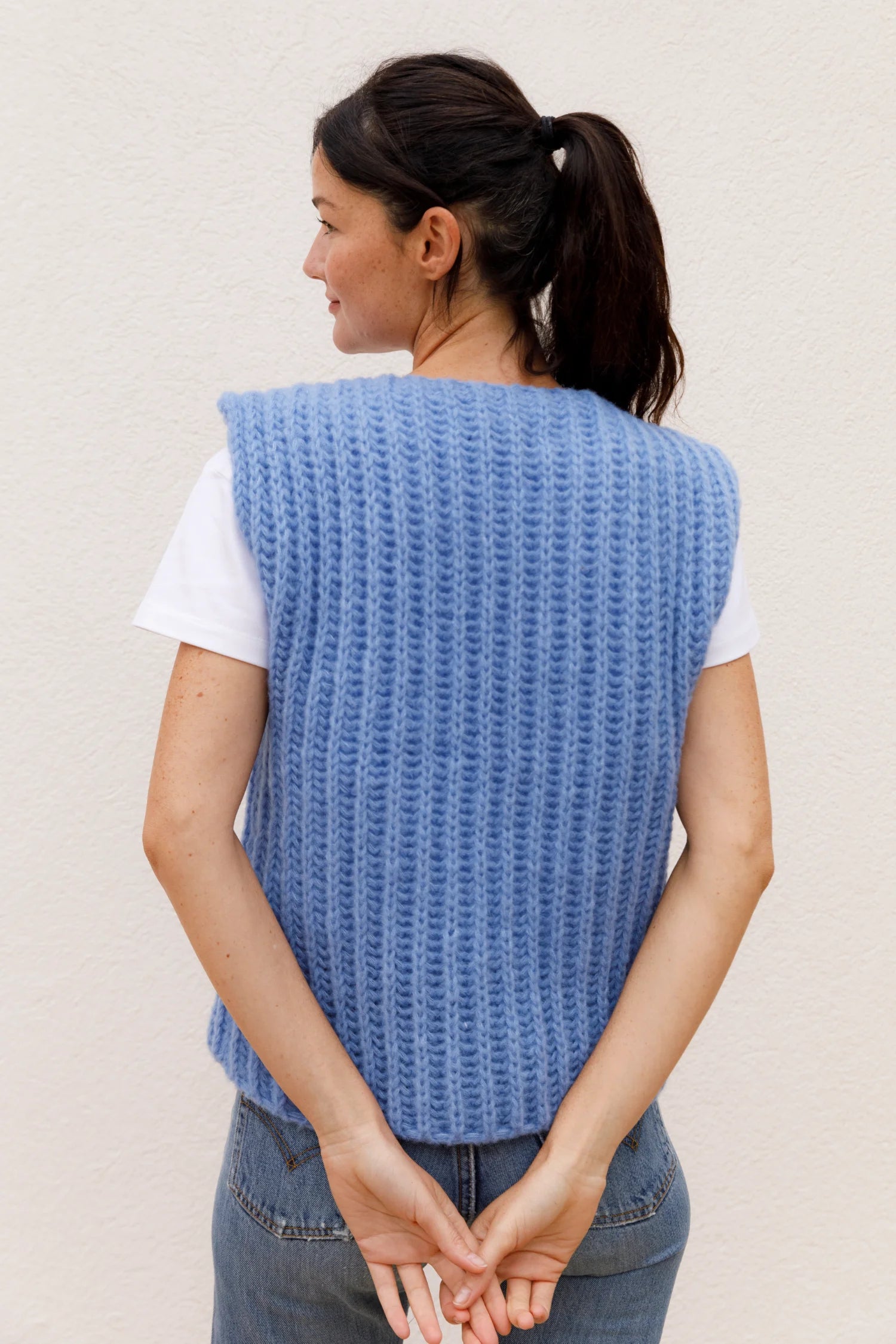 Frau in blauer MYMARINI-Strickweste über weißem T-Shirt, von hinten.#color_capri