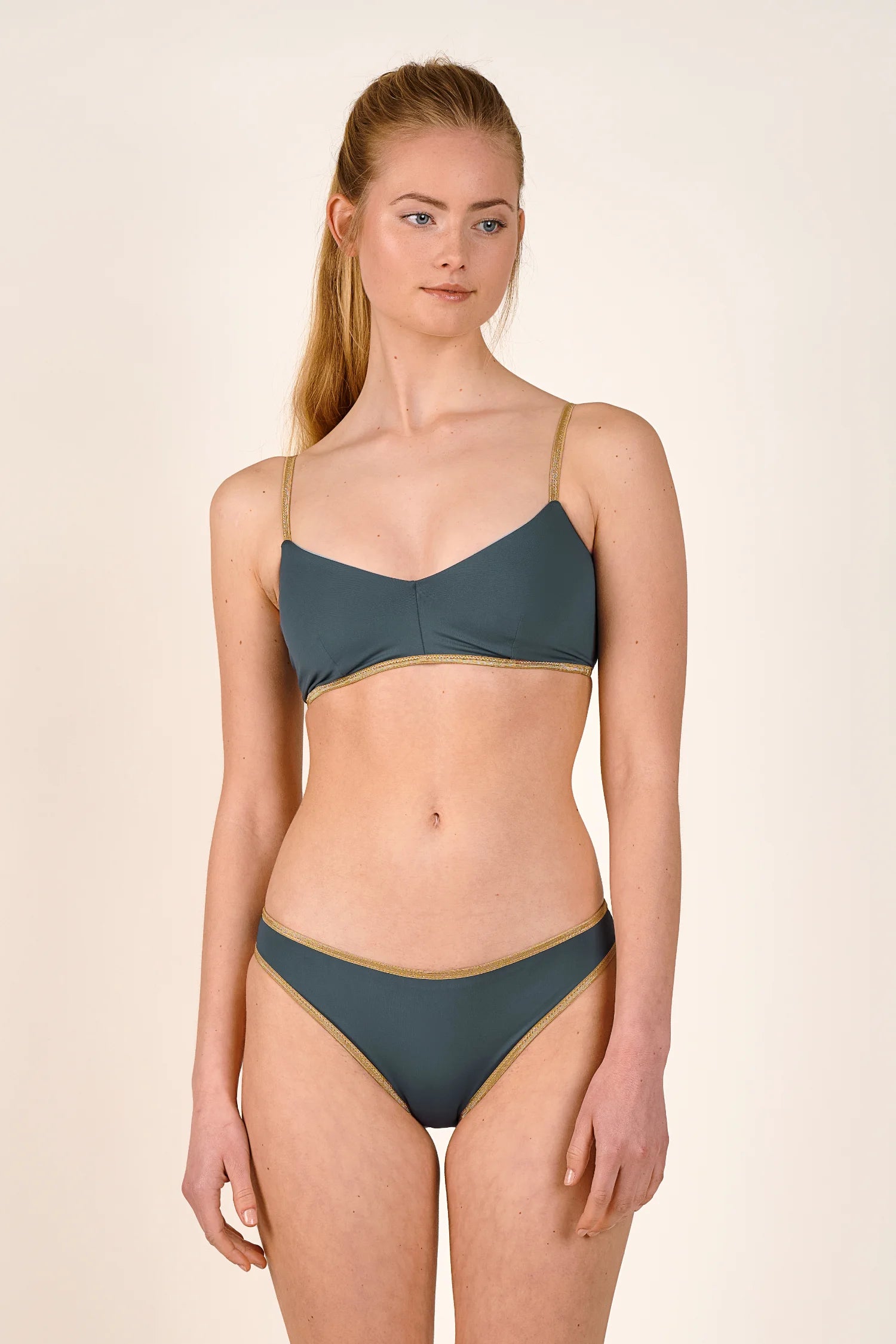 Frau trägt MYMARINI Bikinitop mit Spaghettiträgern und Bikinihose, beide in dunklem Grün mit goldenen Akzenten.#color_crystal-grey