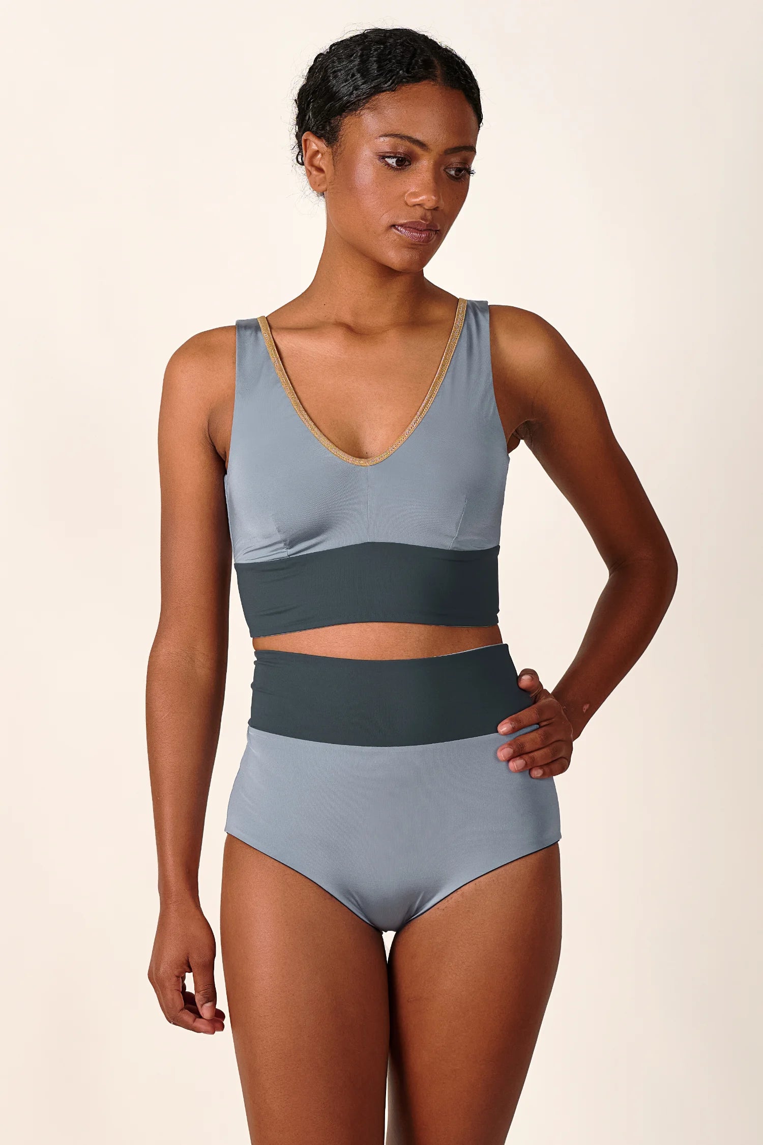 Frau trägt MYMARINI Bikini mit V-Ausschnitt und breiten Trägern in Grau, High-Waist-Schnitt, vor neutralem Hintergrund.#color_crystal-grey