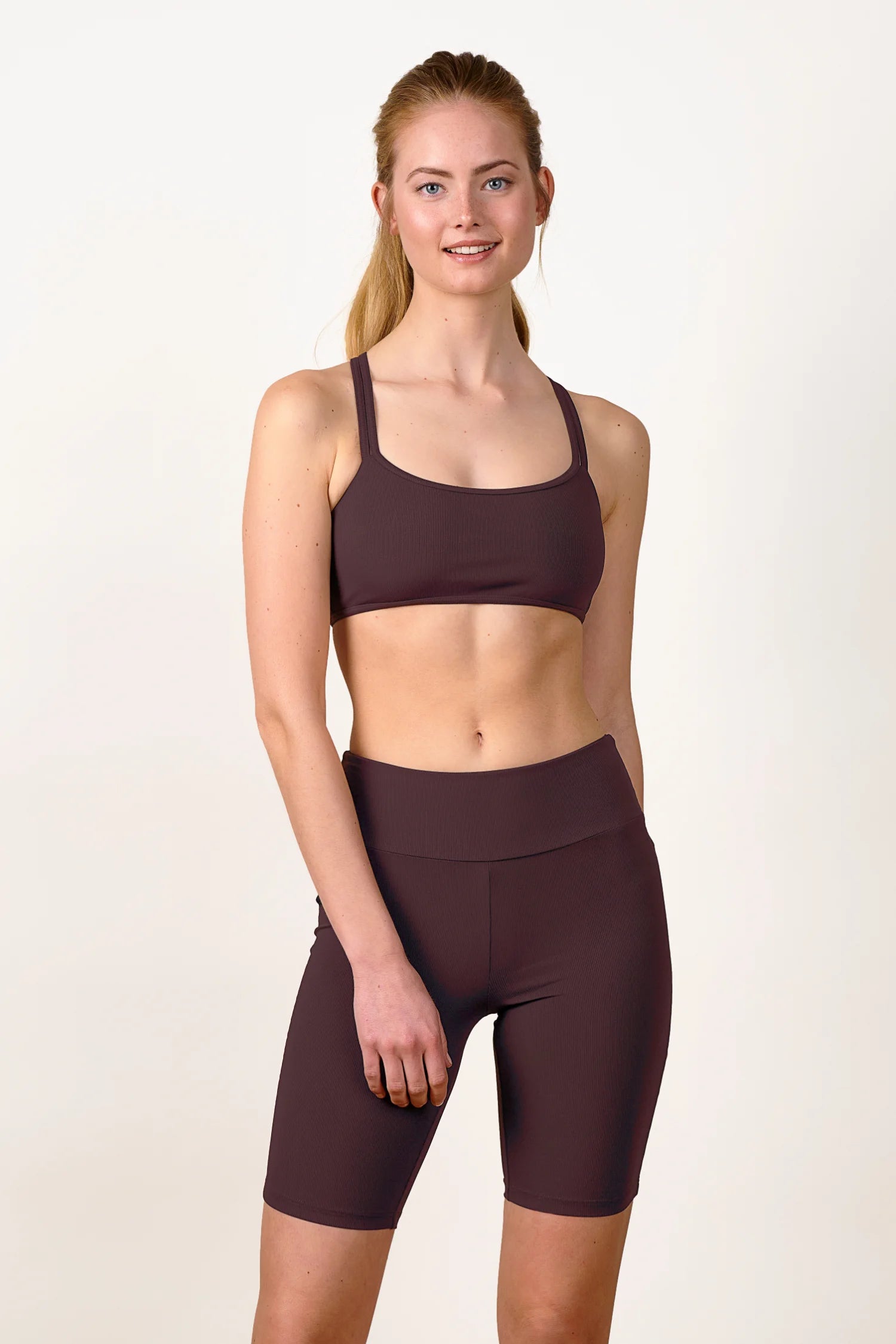 Frau trägt MYMARINI Bikinitop mit breiten Trägern und High-Waist-Shorts in Dunkelbraun, lächelnd vor neutralem Hintergrund.#color_chocolate