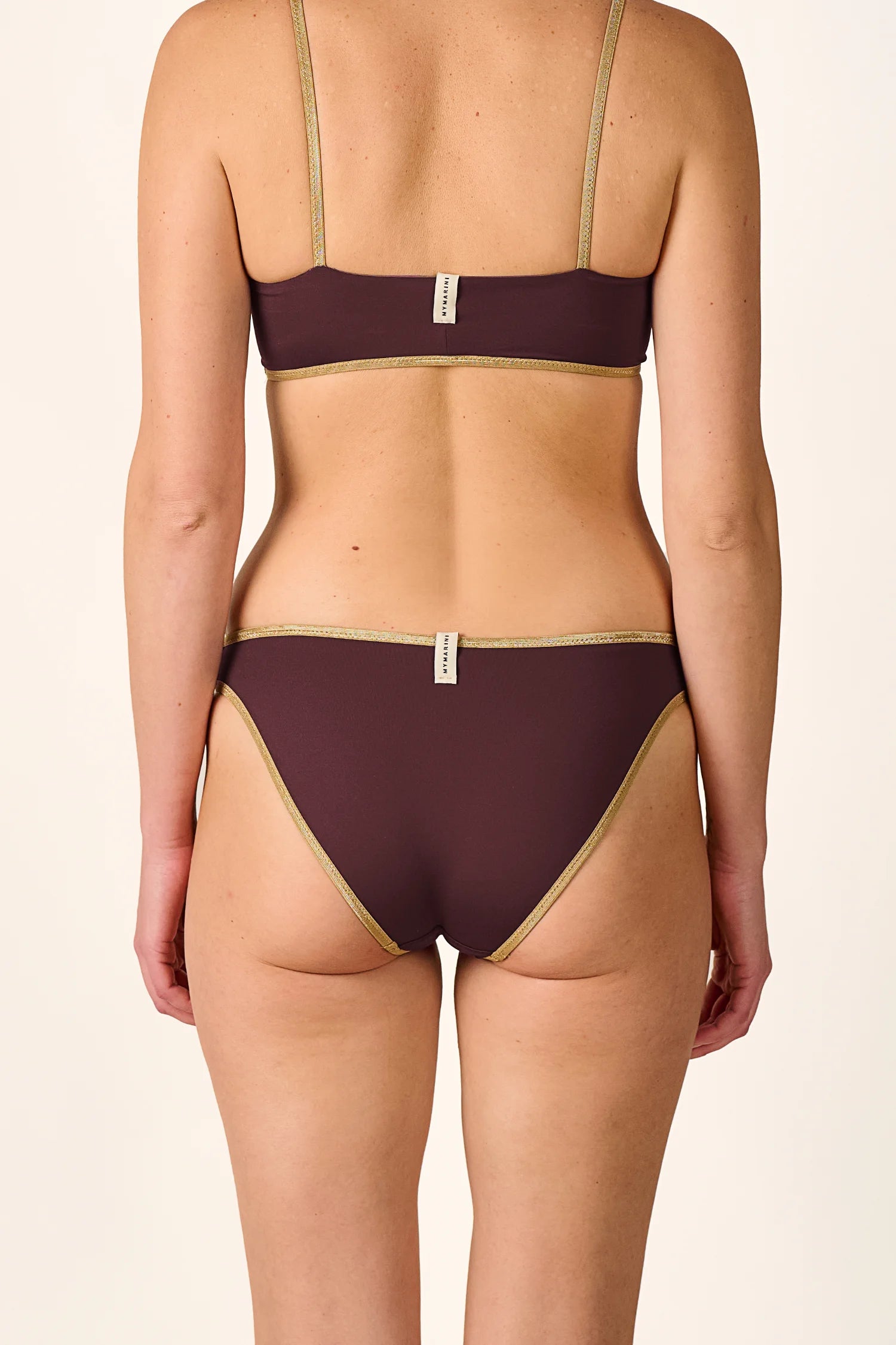 Bikinihose von MYMARINI in dunklem Braun mit goldenen Details, mittelhoher Beinausschnitt, von hinten sichtbar.#color_shimmer-brown
