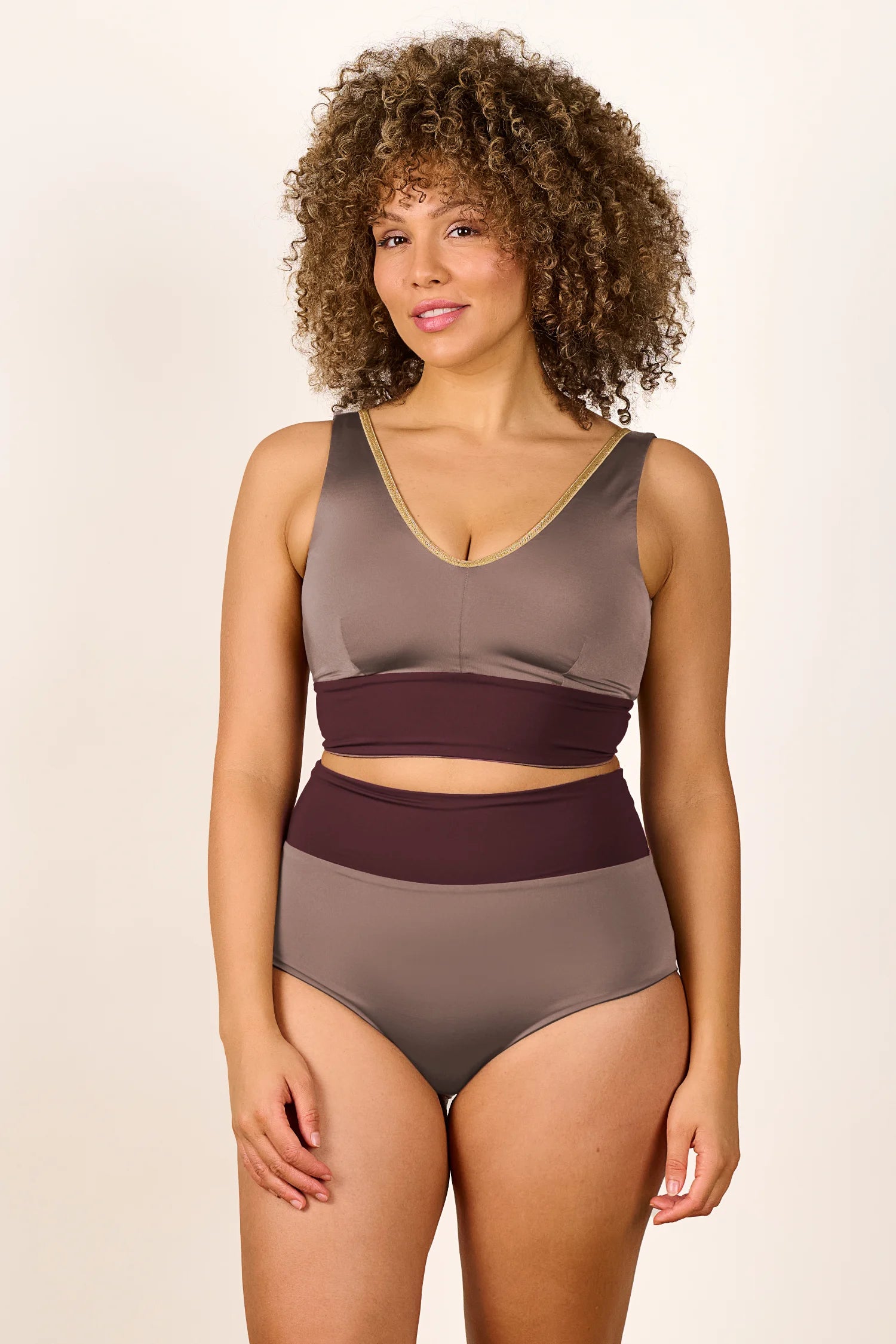 Frau trägt MYMARINI Bikini mit V-Ausschnitt und High Waist Hose in Braun- und Beigetönen, vor neutralem Hintergrund.#color_shimmer-brown