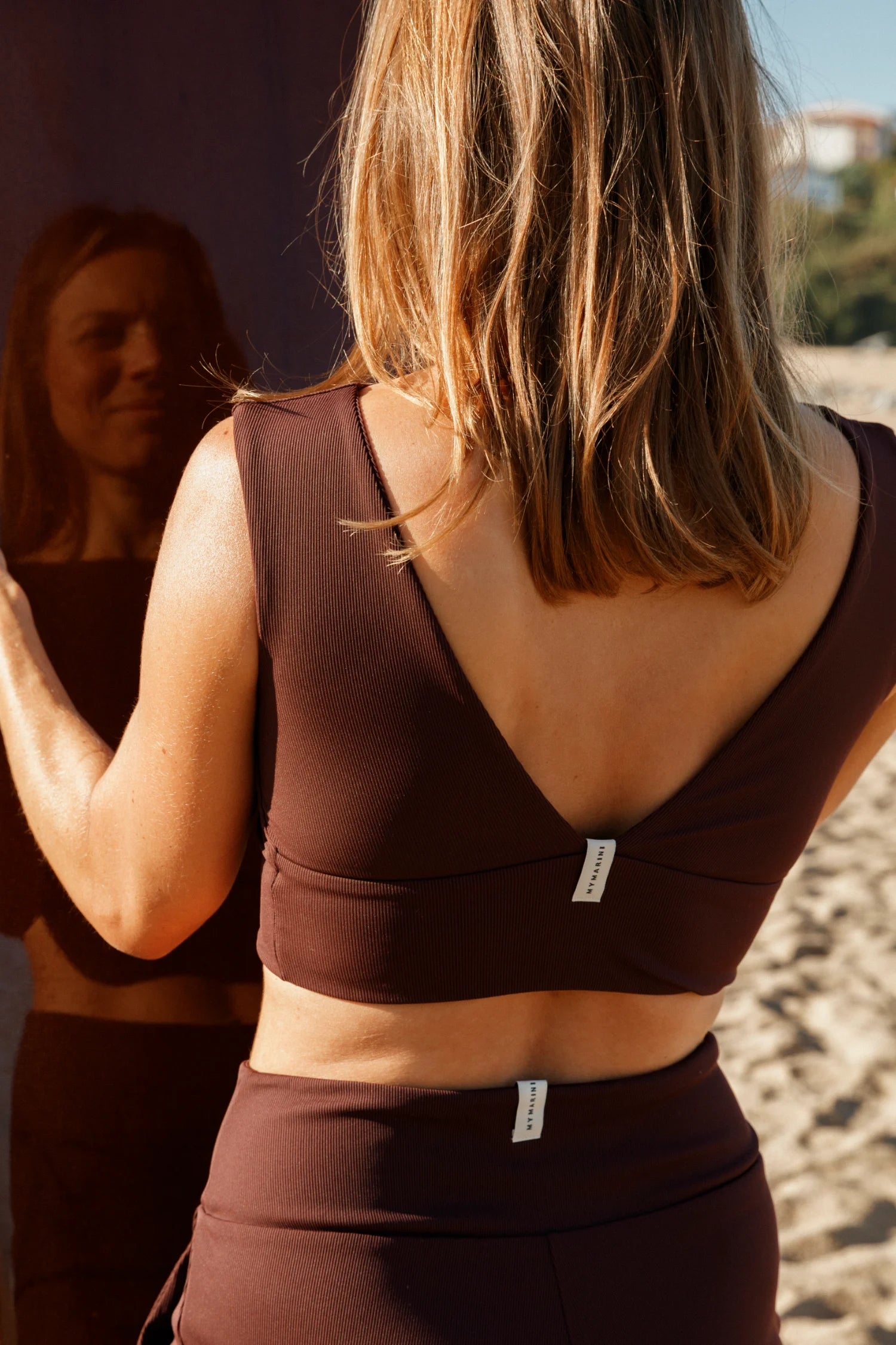 Frau am Strand in braunem MYMARINI Bikinitop mit V-Ausschnitt und passender Bikinihose.#color_chocolate