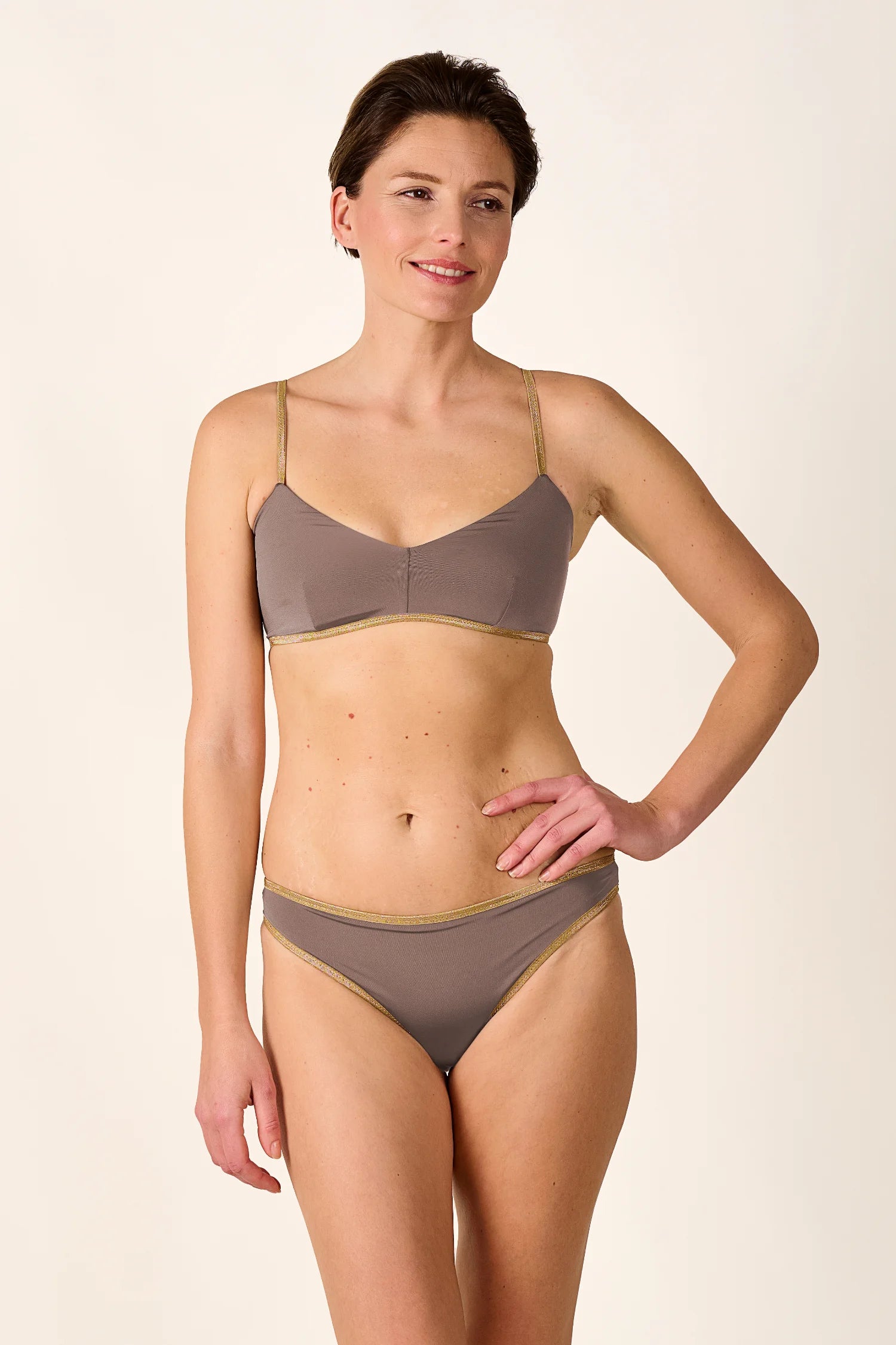 Frau trägt MYMARINI Bikini mit Spaghettiträgern und hohem Beinausschnitt in Beige.#color_shimmer-brown