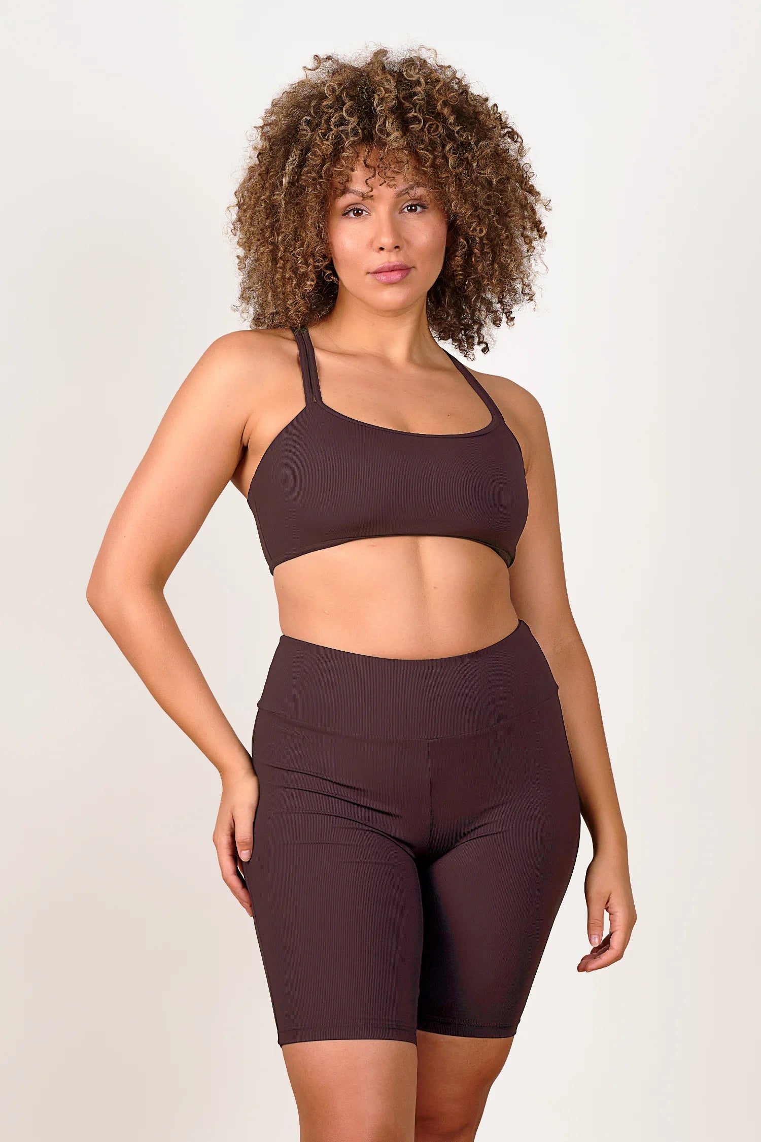 Frau trägt MYMARINI Bikinitop mit breiten Trägern und High-Waist-Bikinihose in Dunkelbraun vor neutralem Hintergrund.#color_chocolate