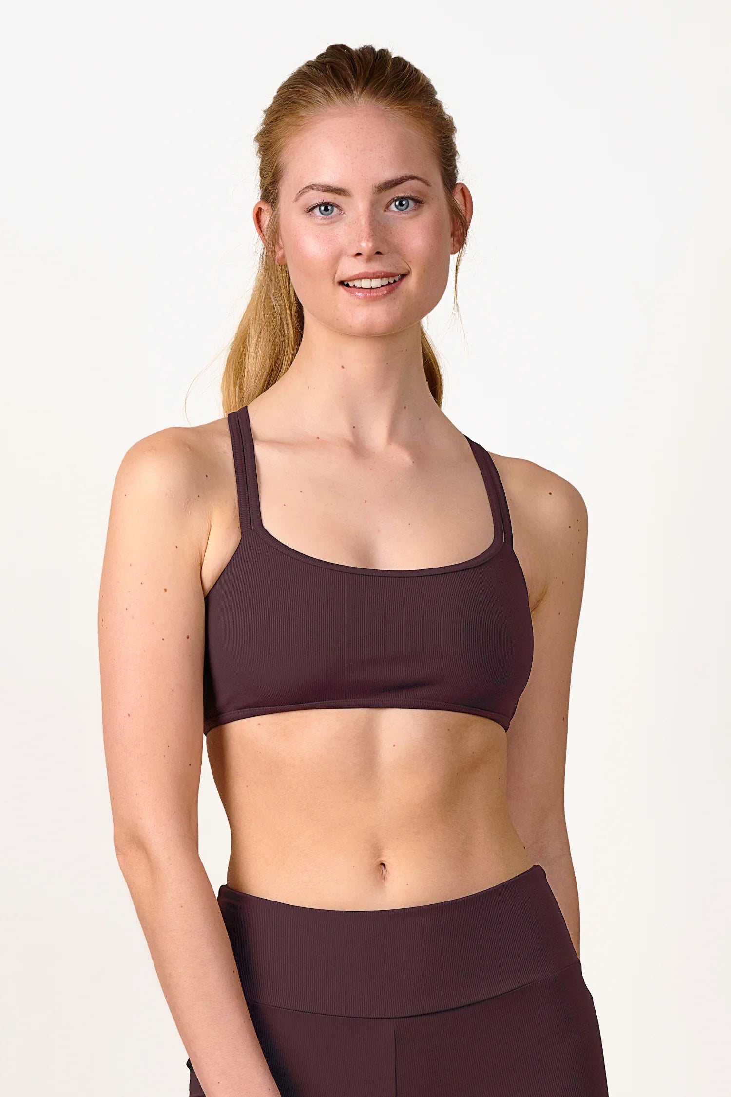 Frau trägt MYMARINI Bikinitop mit breiten Trägern in Dunkelrot, lächelnd vor neutralem Hintergrund.#color_chocolate