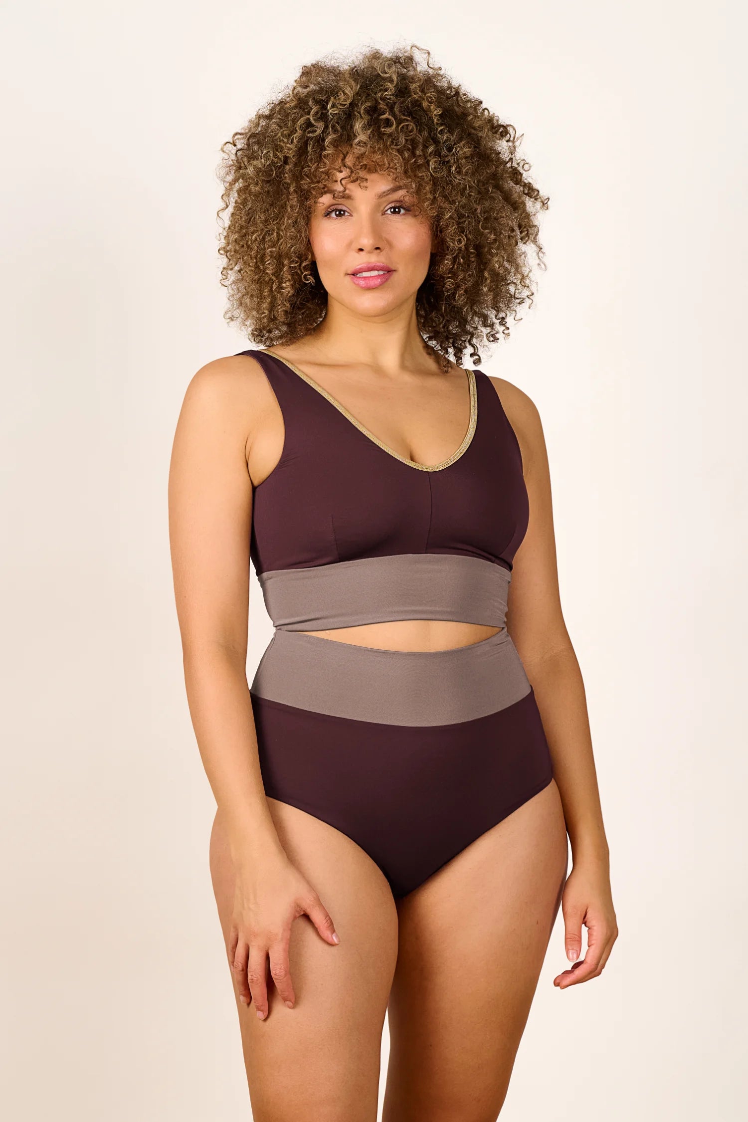 Frau trägt MYMARINI Badeanzug mit V-Ausschnitt und hohem Beinausschnitt in Braun und Beige.#color_shimmer-brown