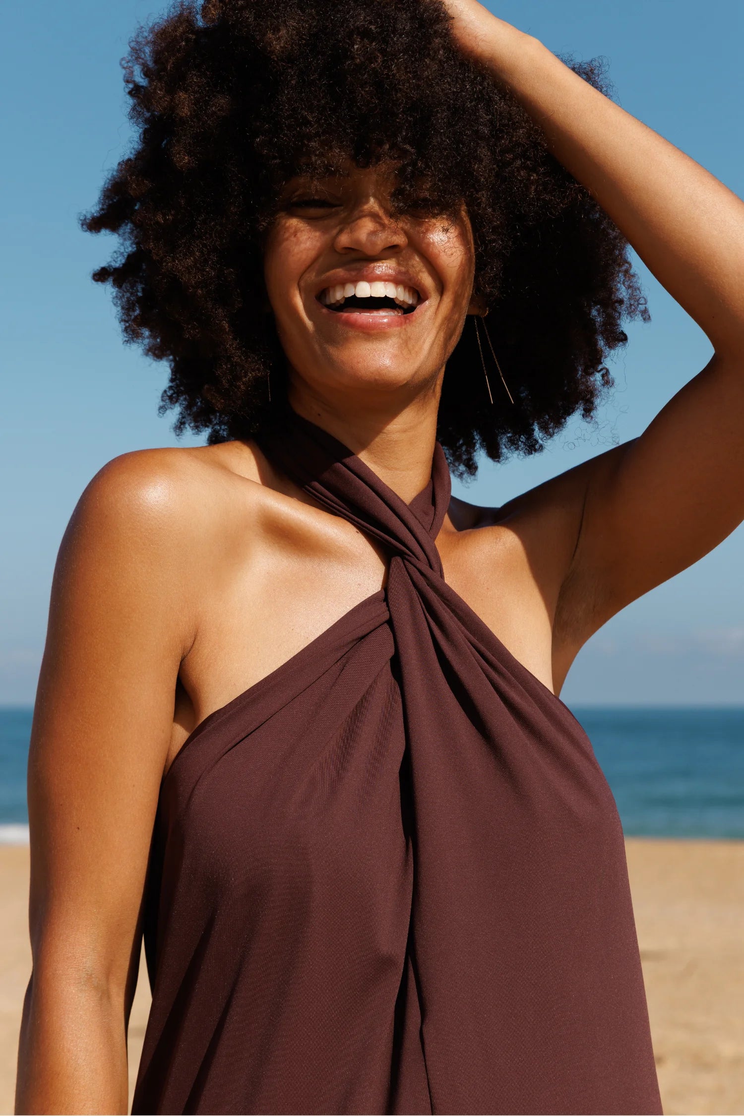 MYMARINI Bikinioberteil in braunem Stoff mit Neckholder-Knoten am Hals; Strand, Meer, lächelnde Frau.#color_chocolate