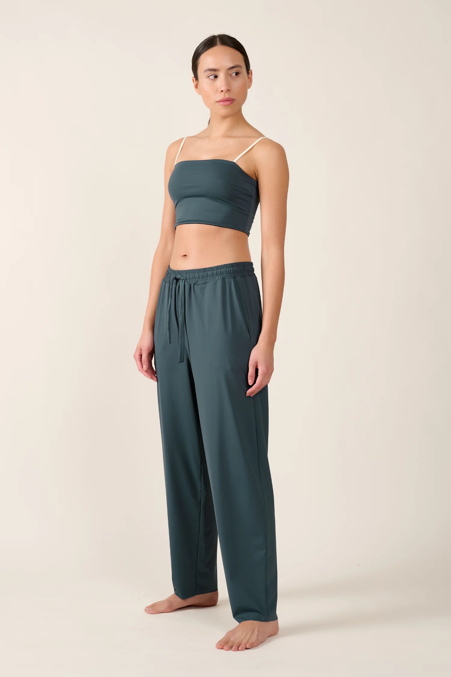 Person trägt MYMARINI Bikinitop mit Spaghettiträgern und Hose in Dunkelgrün, steht vor neutralem Hintergrund.#color_grey