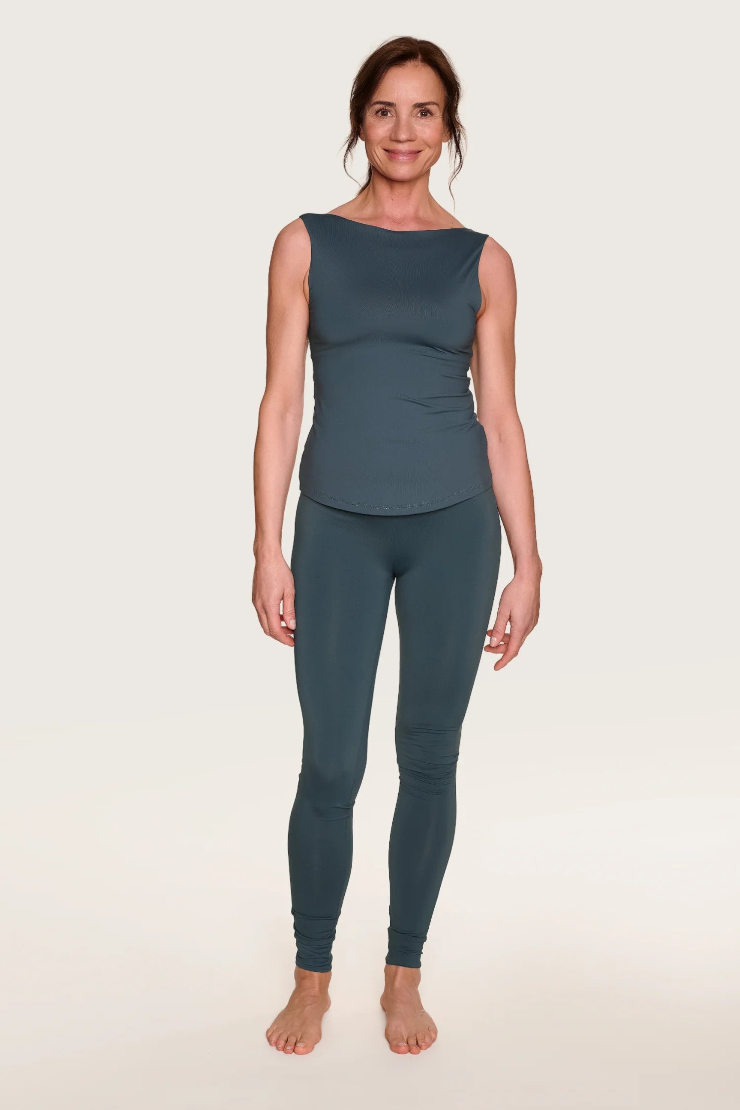 Frau trägt MYMARINI Top mit breiten Trägern und Leggings in Dunkelblau, stehend vor hellem Hintergrund.#color_grey