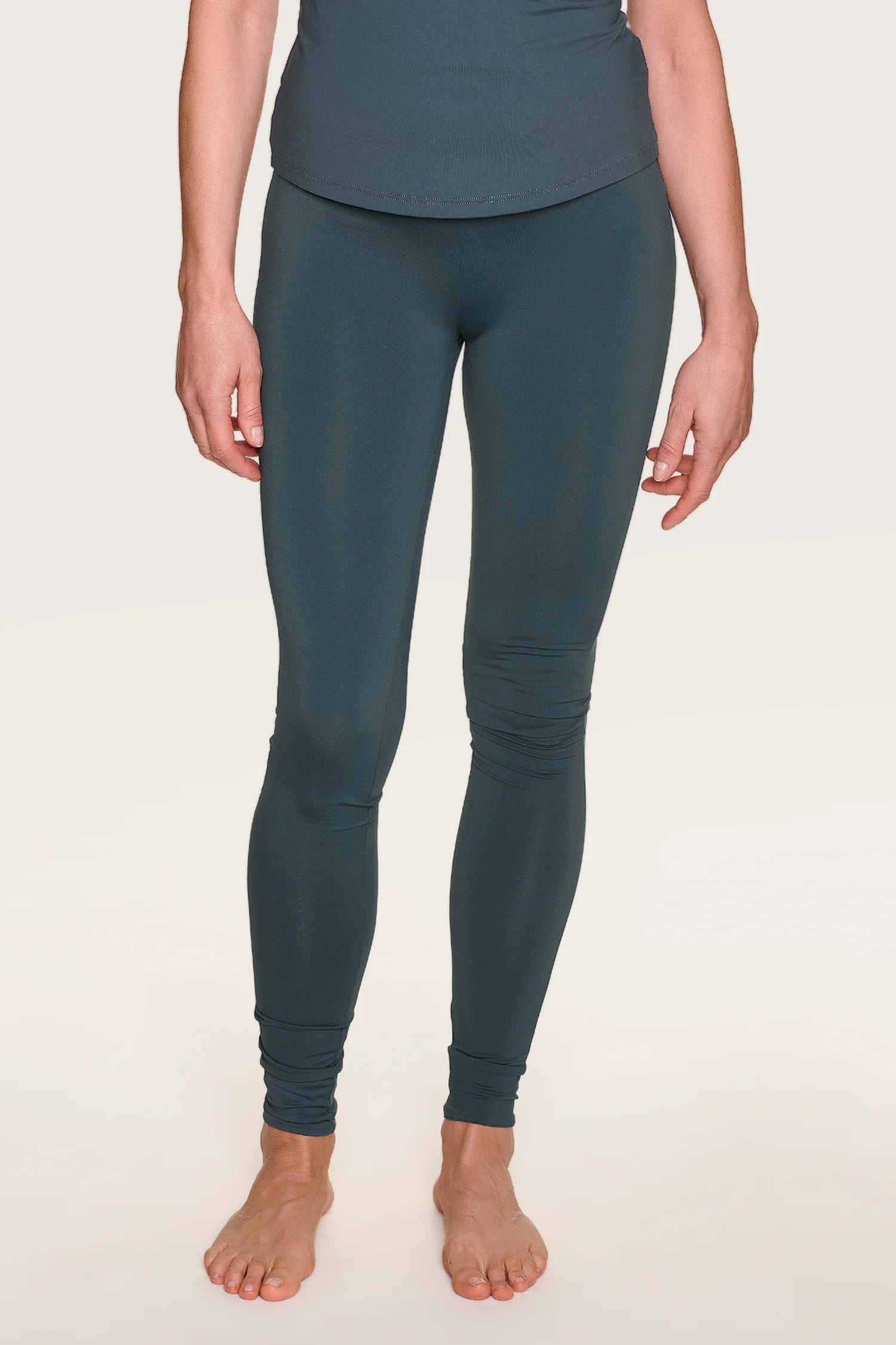 Person trägt MYMARINI-Leggings in Dunkelgrün, eng anliegend, knöchellang, barfuß stehend vor neutralem Hintergrund.#color_grey