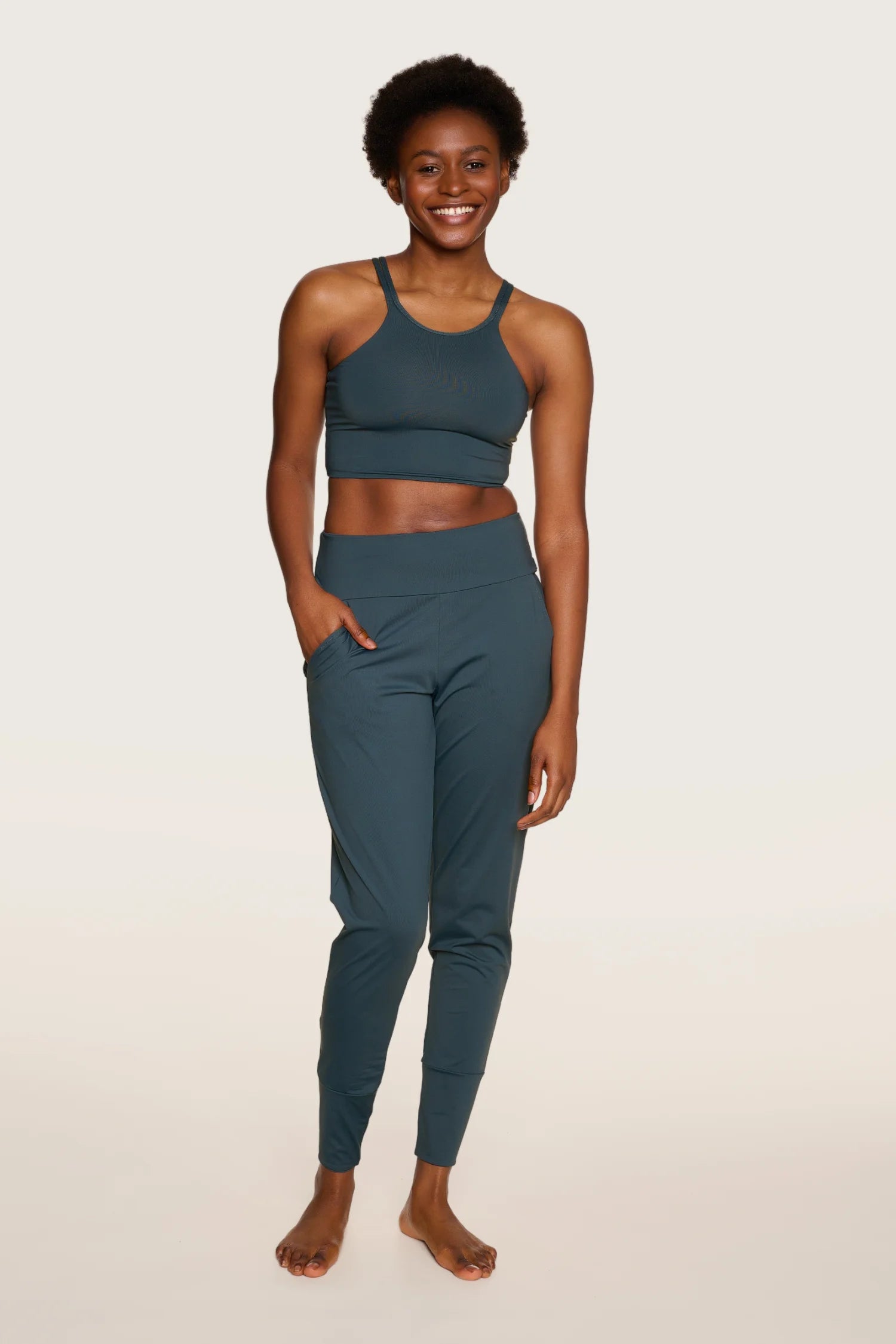 Frau trägt MYMARINI Top mit breiten Trägern und Hose in Dunkelgrün, lächelnd, vor hellem Hintergrund.#color_grey