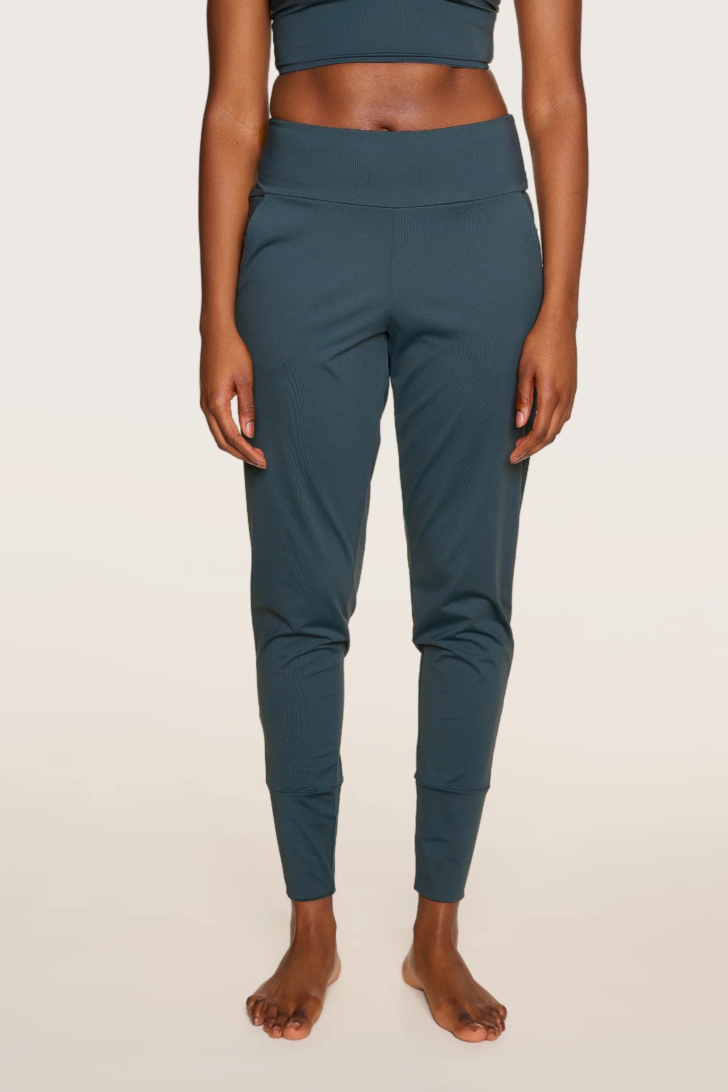 Person trägt MYMARINI-Hose in Dunkelgrün, stehend, mit breitem Bund und schmalem Schnitt, vor hellem Hintergrund.#color_grey