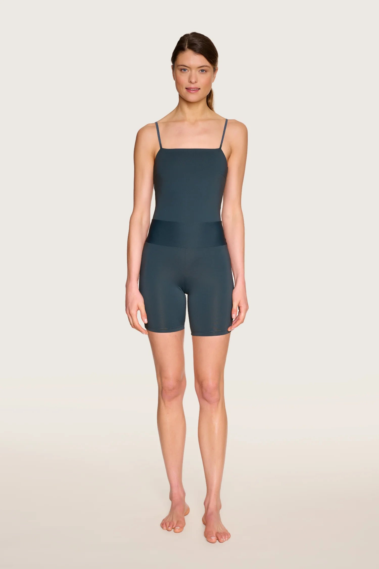 Frau trägt MYMARINI One-Piece mit Spaghettiträgern, hoch geschlossenem Schnitt, in dunklem Farbton, vor hellem Hintergrund.#color_grey