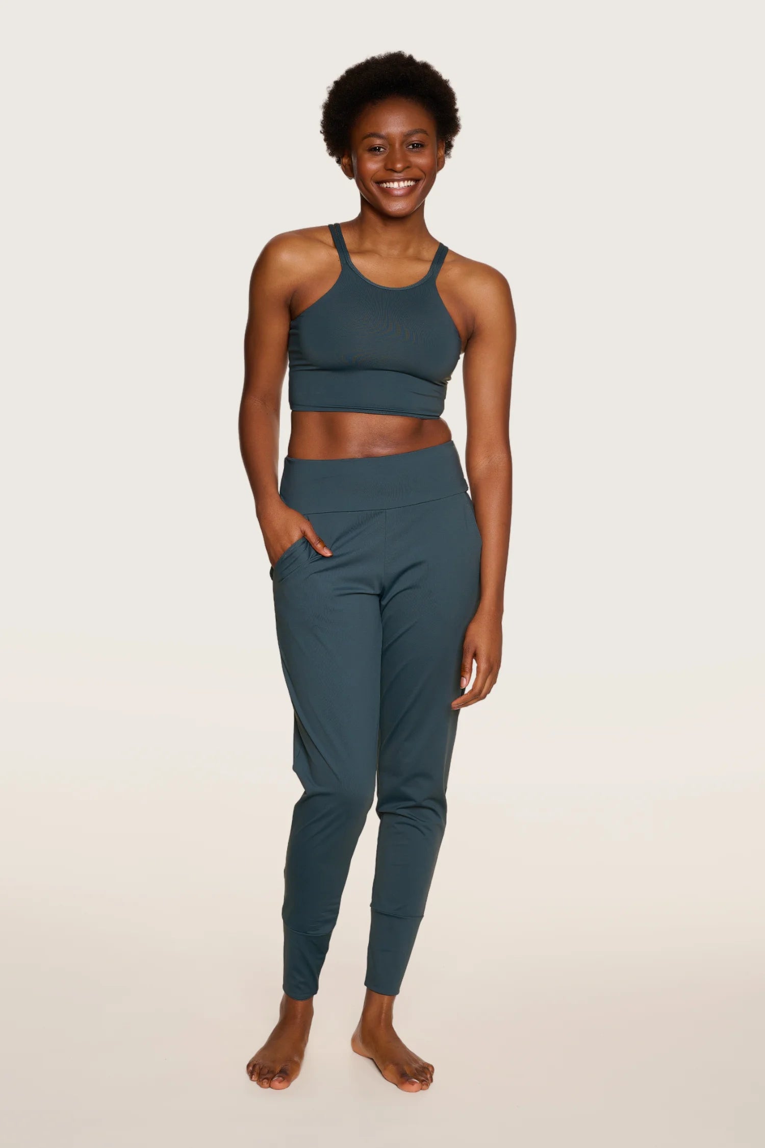 Frau trägt MYMARINI Top mit breiten Trägern und Hose in Dunkelblau, lächelnd, vor hellem Hintergrund.#color_grey