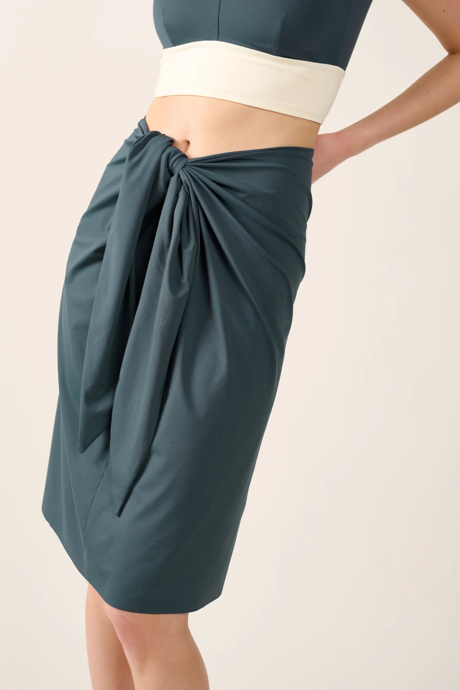 Person trägt einen MYMARINI Rock in Dunkelgrün mit Knoten-Detail vorne.#color_grey