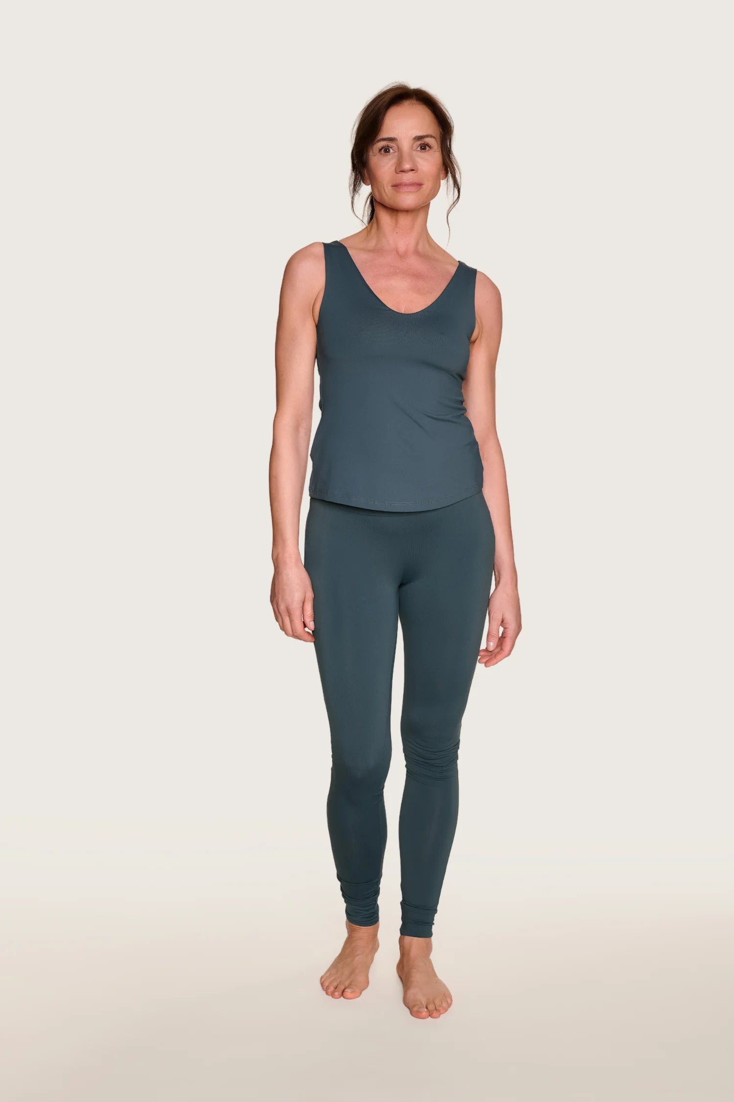 Frau trägt MYMARINI Top mit V-Ausschnitt und Leggings in Dunkelgrün, stehend vor hellem Hintergrund.#color_grey