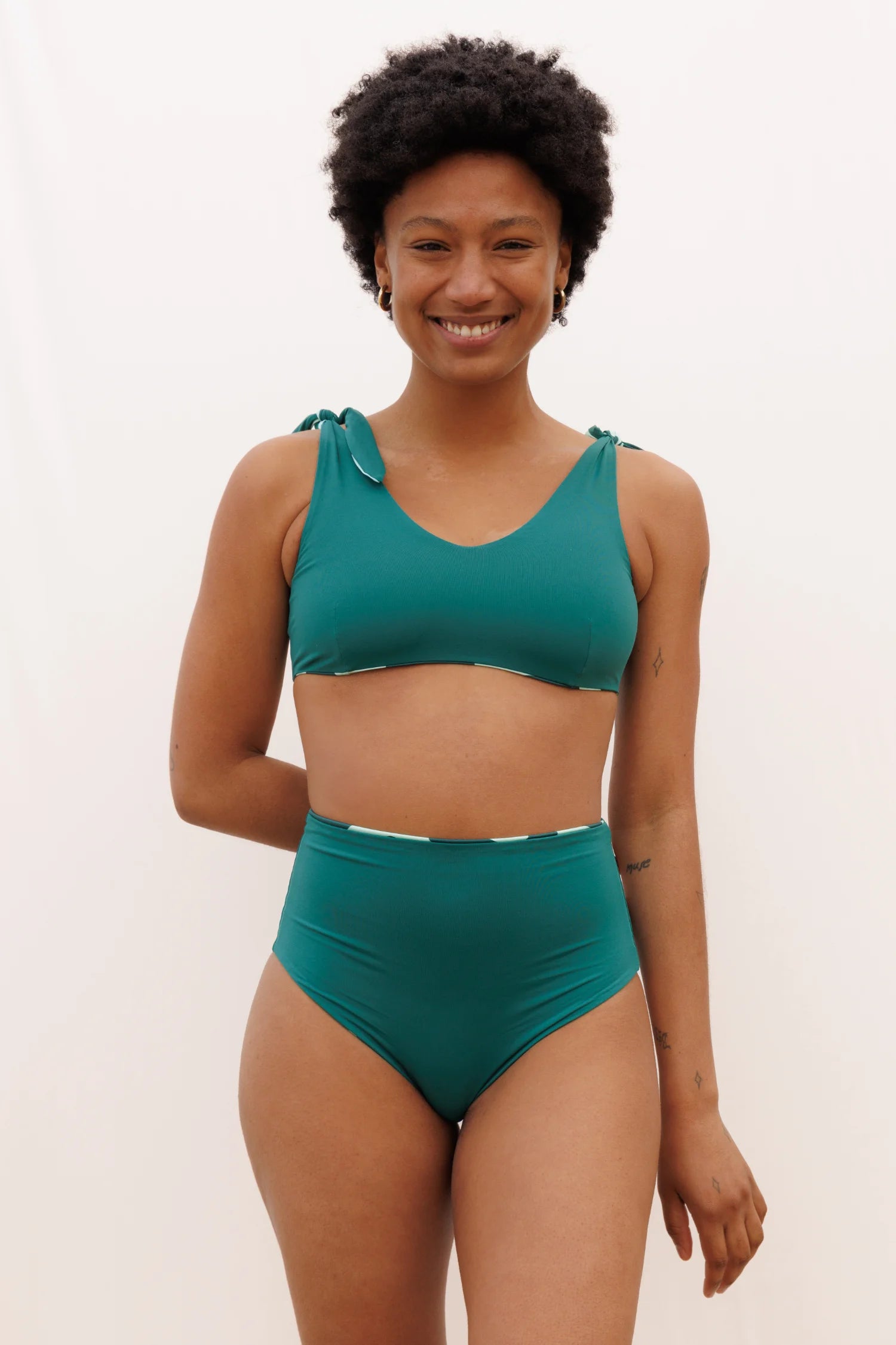 Bikinioberteil und -hose von MYMARINI in Grün mit breiten Trägern und hohem Beinausschnitt, lächelnde Person im Vordergrund.#color_jungle-print