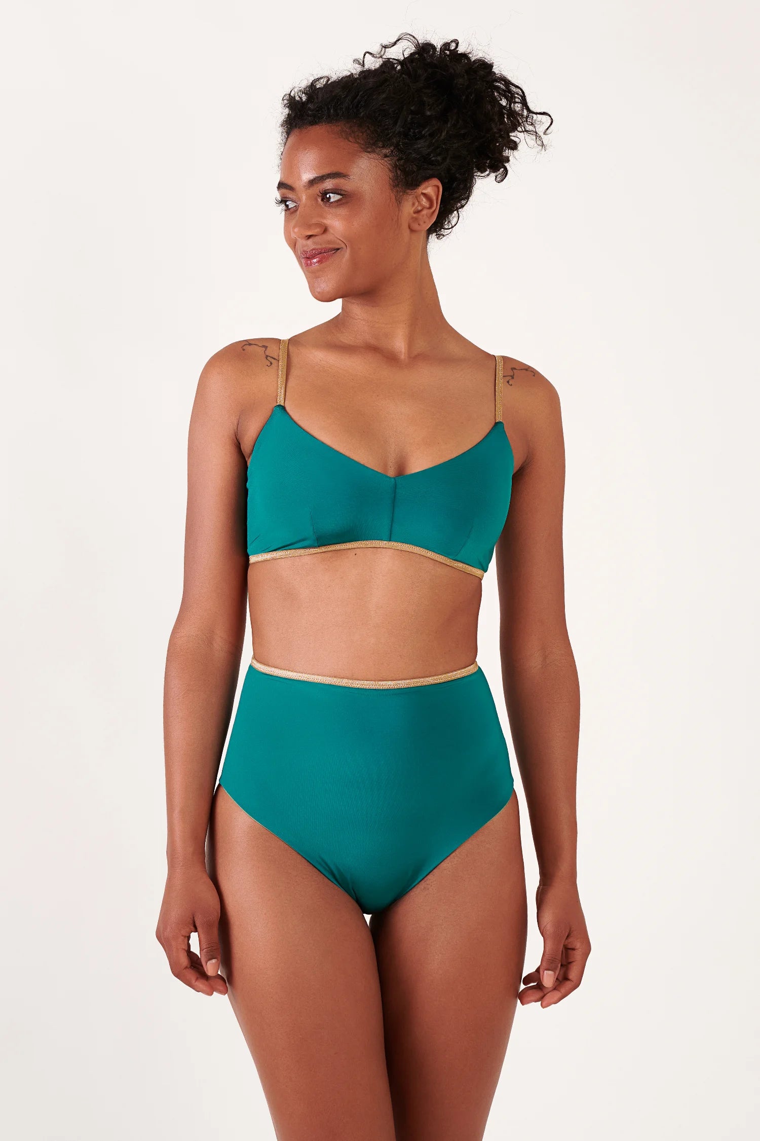 Frau trägt MYMARINI Bikini in tealfarbenem Ton mit goldenen Zierkanten; Oberteil mit Spaghettiträgern, High-Waist-Hose, goldener Rand.#color_pine-basil