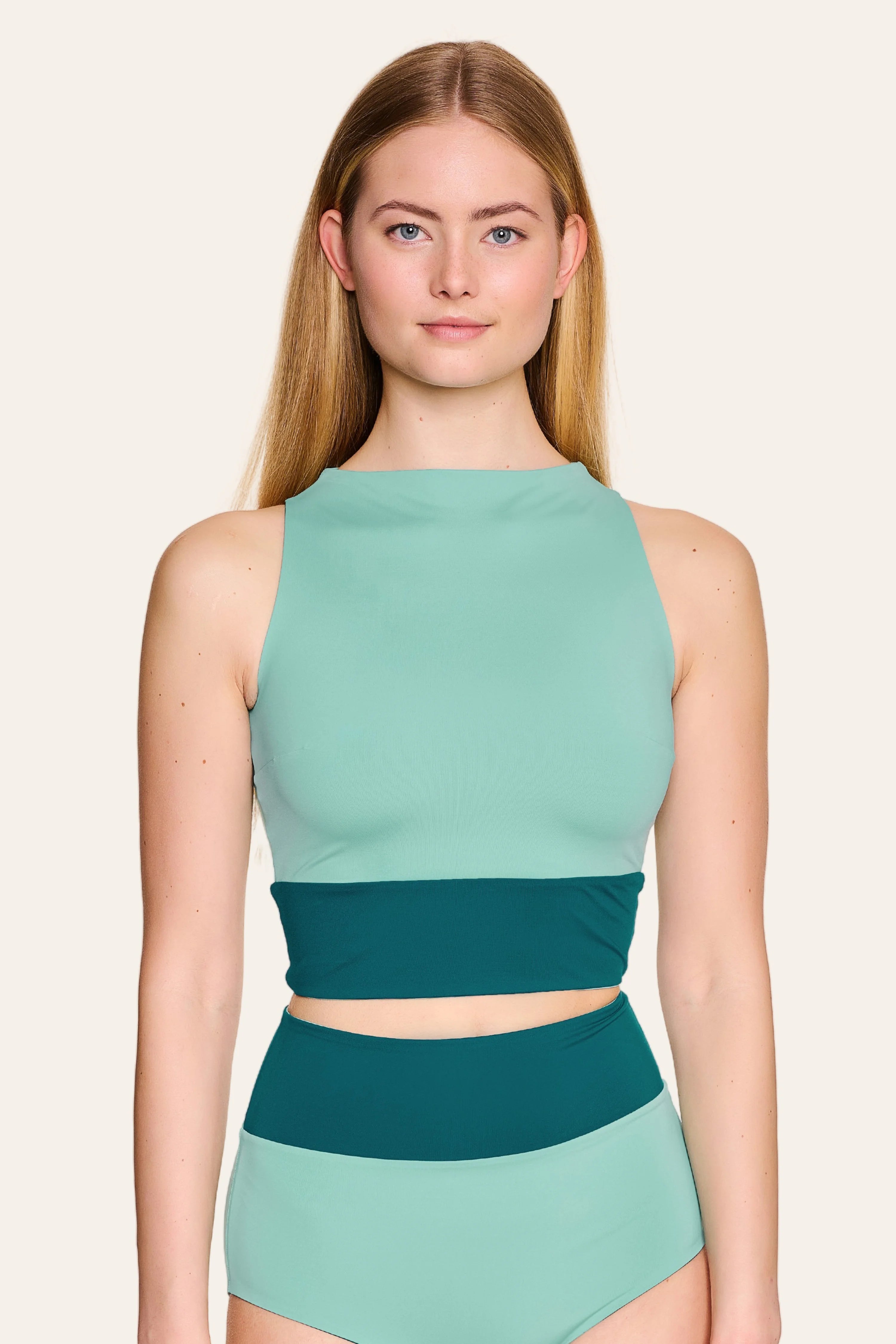 Frau trägt MYMARINI Badeanzug mit hochgeschlossenem Schnitt und hohem Beinausschnitt in Mintgrün und Dunkelgrün.#color_eucalyptus-petrol