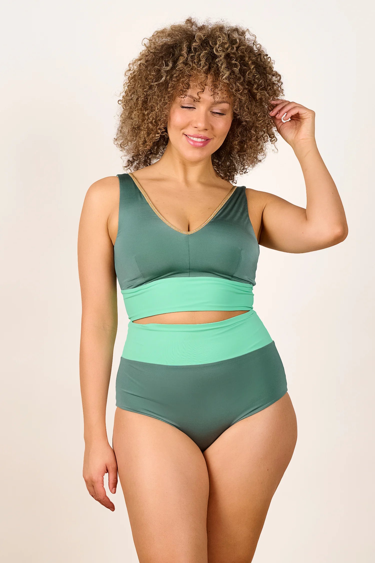 Frau trägt MYMARINI Bikini mit V-Ausschnitt und High Waist in Grüntönen, lächelnd vor neutralem Hintergrund.#color_lagoon-teal