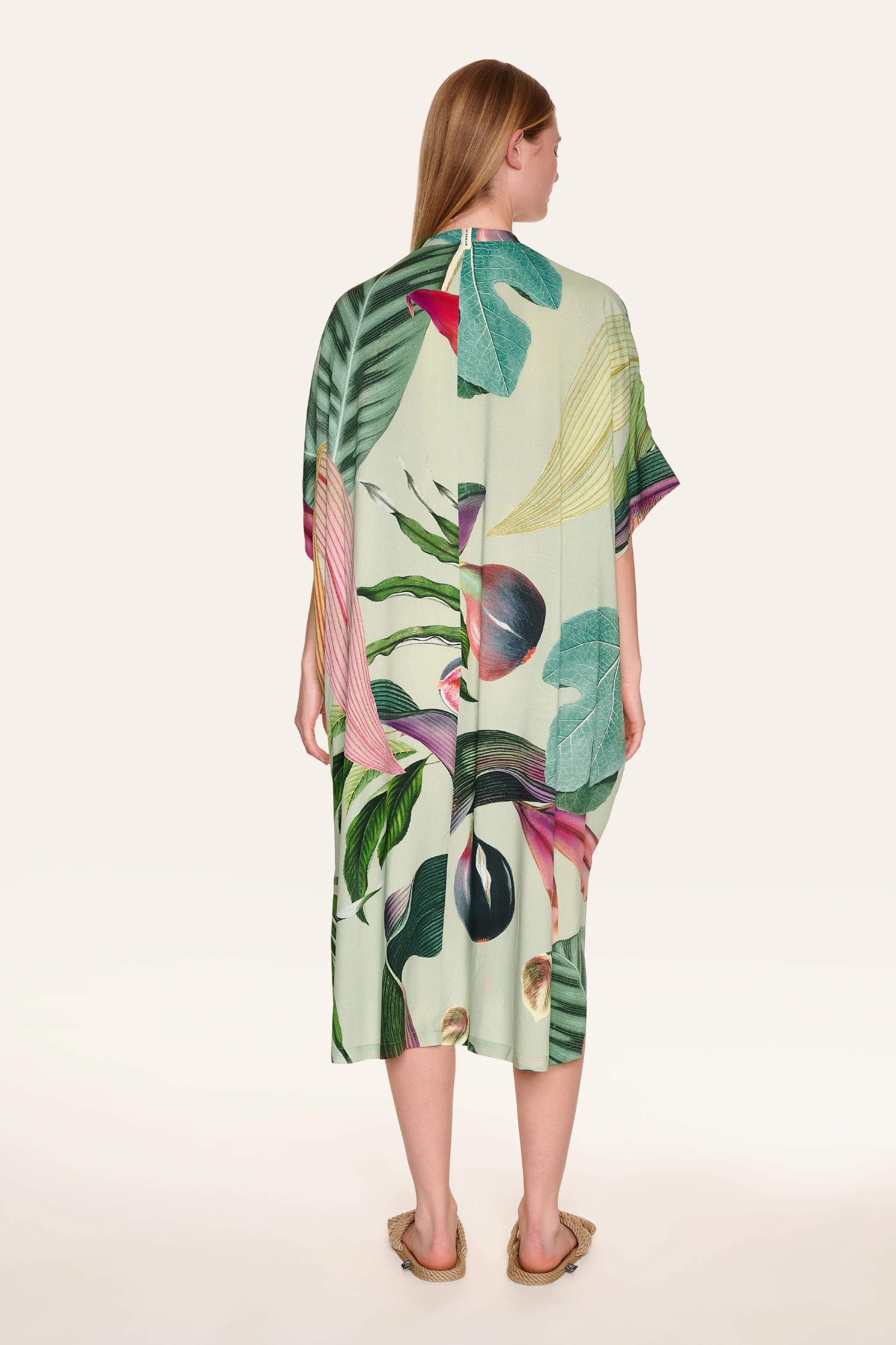 Person von hinten in einem MYMARINI-Kleid mit tropischem Muster, knielang, lockerer Schnitt, kurze Ärmel.#color_tropical-print