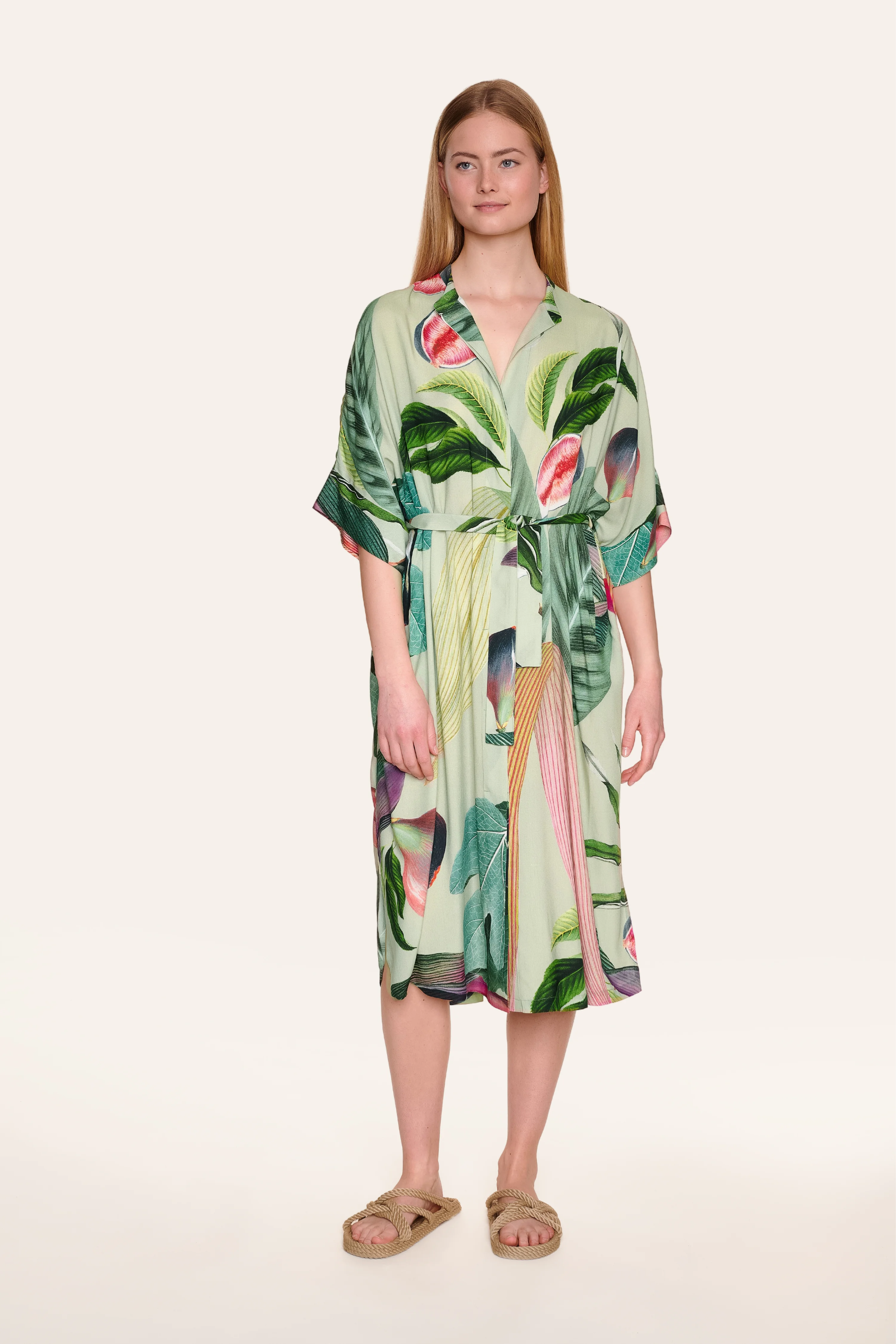 Frau trägt MYMARINI-Kleid mit tropischem Muster und Gürtel, knielang, mit kurzen Ärmeln.#color_tropical-print
