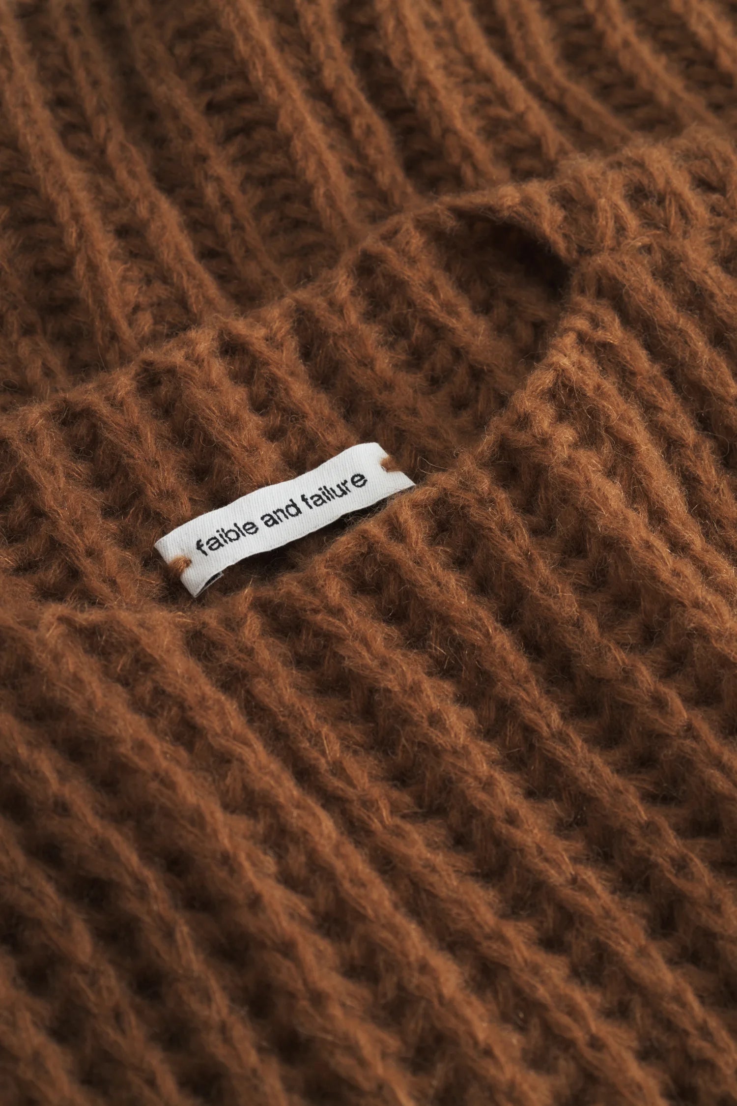 Brauner Strickpullover mit sichtbarem Etikett von "fable and failure".#color_camel