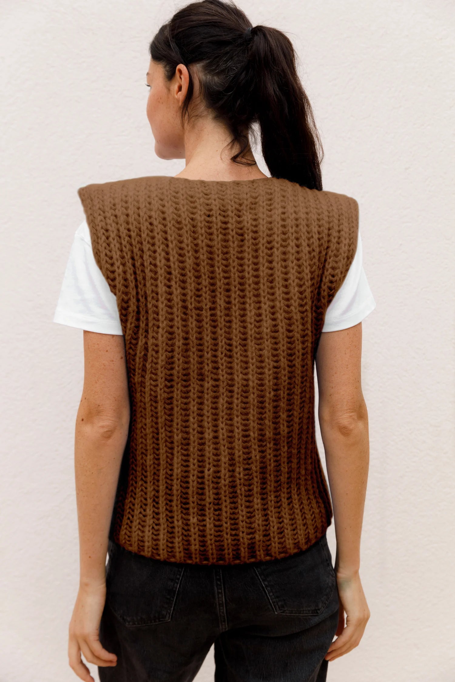 Frau von hinten in braunem MYMARINI-Top mit breiten Trägern über weißem T-Shirt, vor hellem Hintergrund.#color_camel