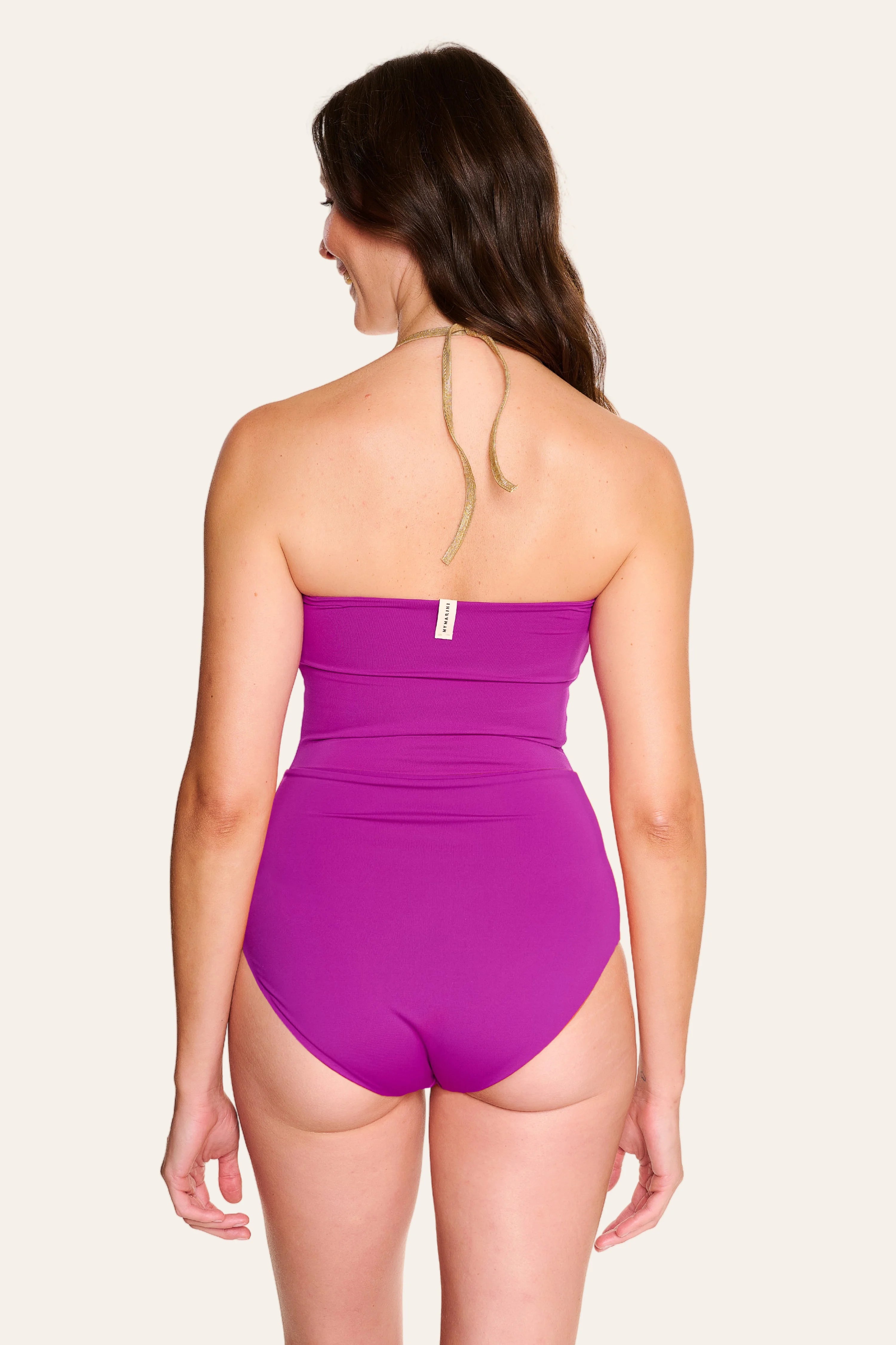 Frau in lila MYMARINI Badeanzug mit Bandeau-Schnitt und hohem Beinausschnitt, von hinten gezeigt.#color_papaya-cassis