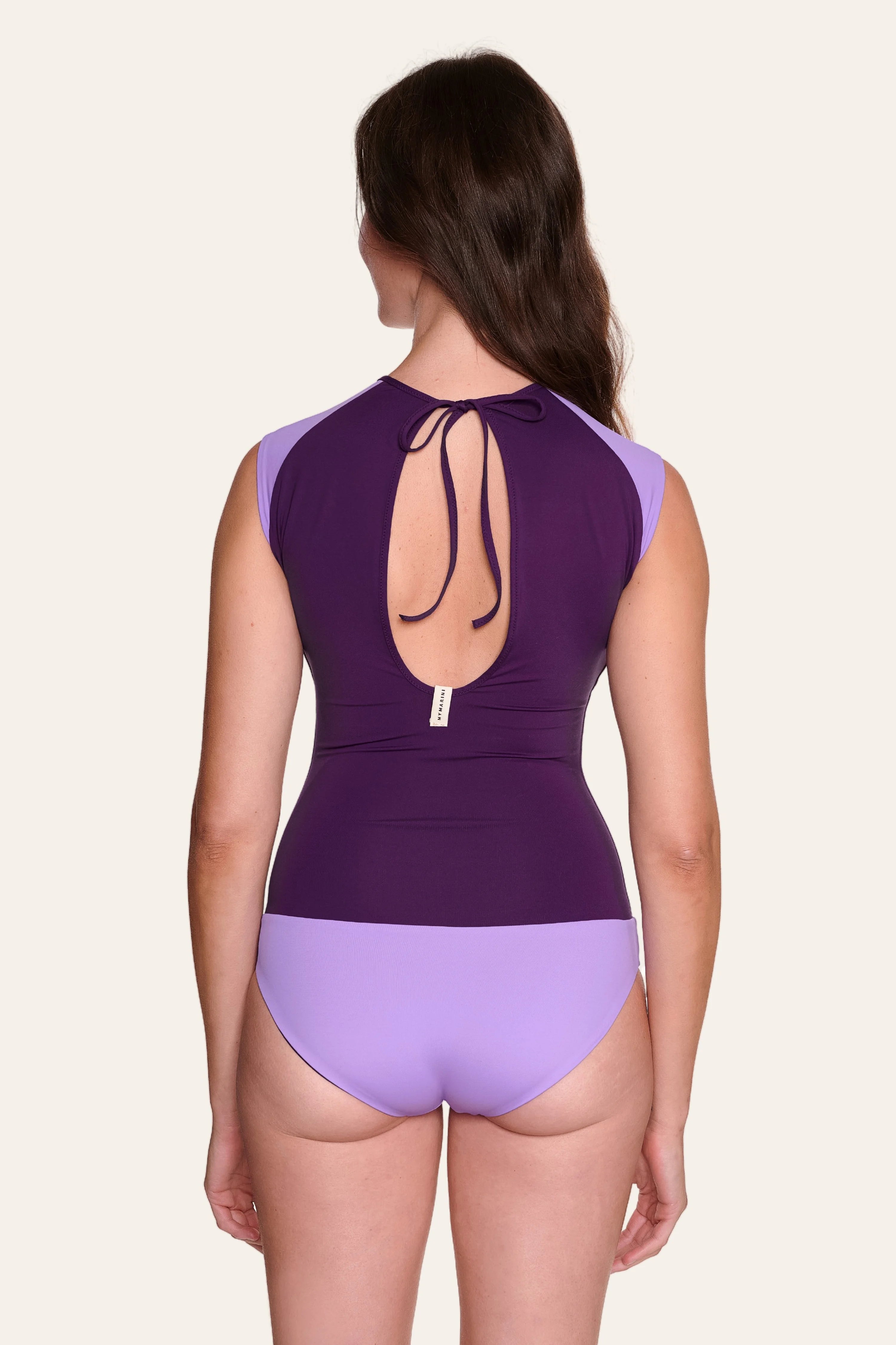 Frau in lila MYMARINI Badeanzug mit tiefem Rückenausschnitt und breiten Trägern, von hinten gezeigt.#color_lavender-plum