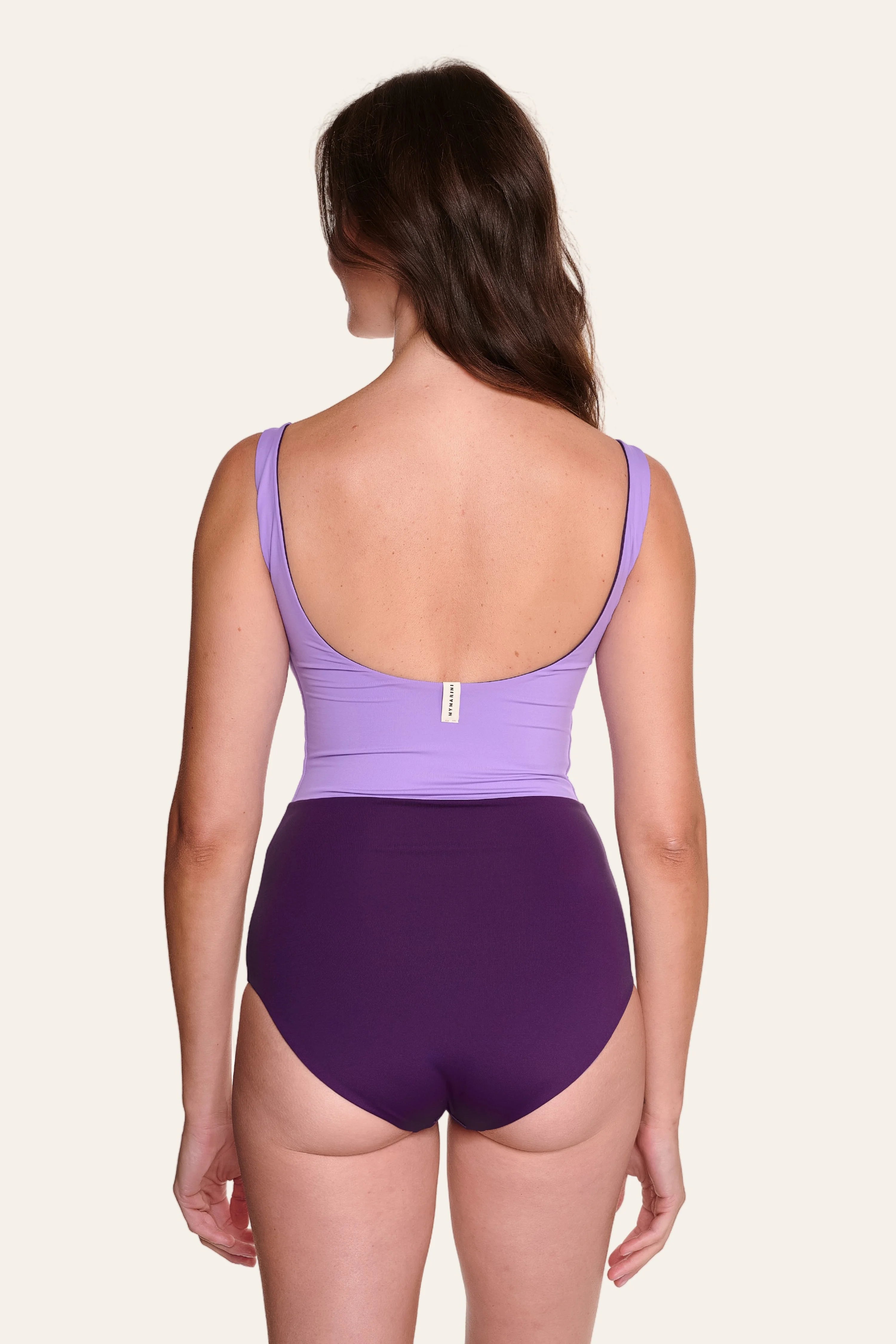 Frau in lila MYMARINI Badeanzug mit tiefem Rückenausschnitt und breiten Trägern, von hinten gezeigt.#color_lavender-plum