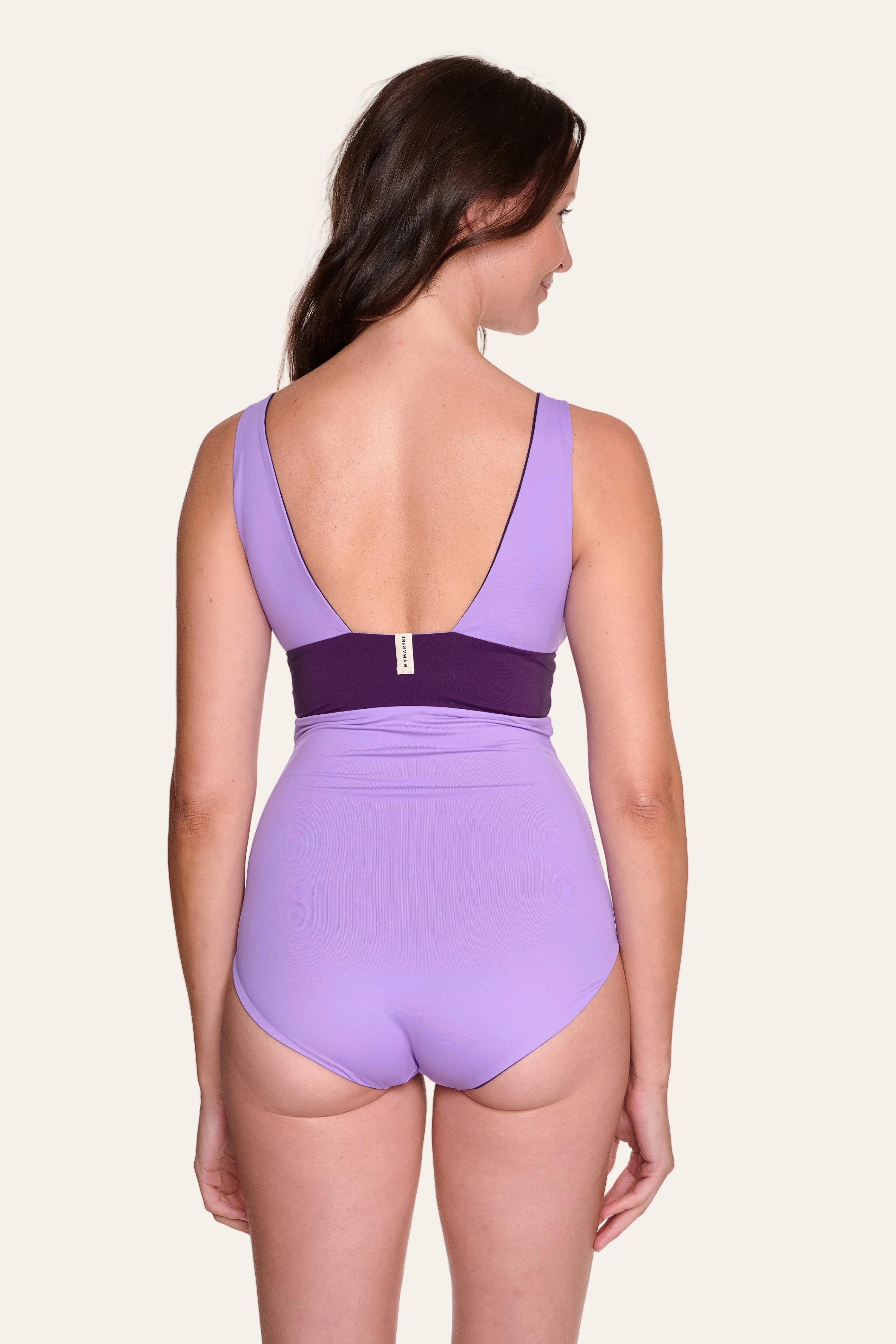 Frau im lila MYMARINI Badeanzug mit tiefem Rückenausschnitt und breiten Trägern, von hinten gezeigt.#color_lavender-plum